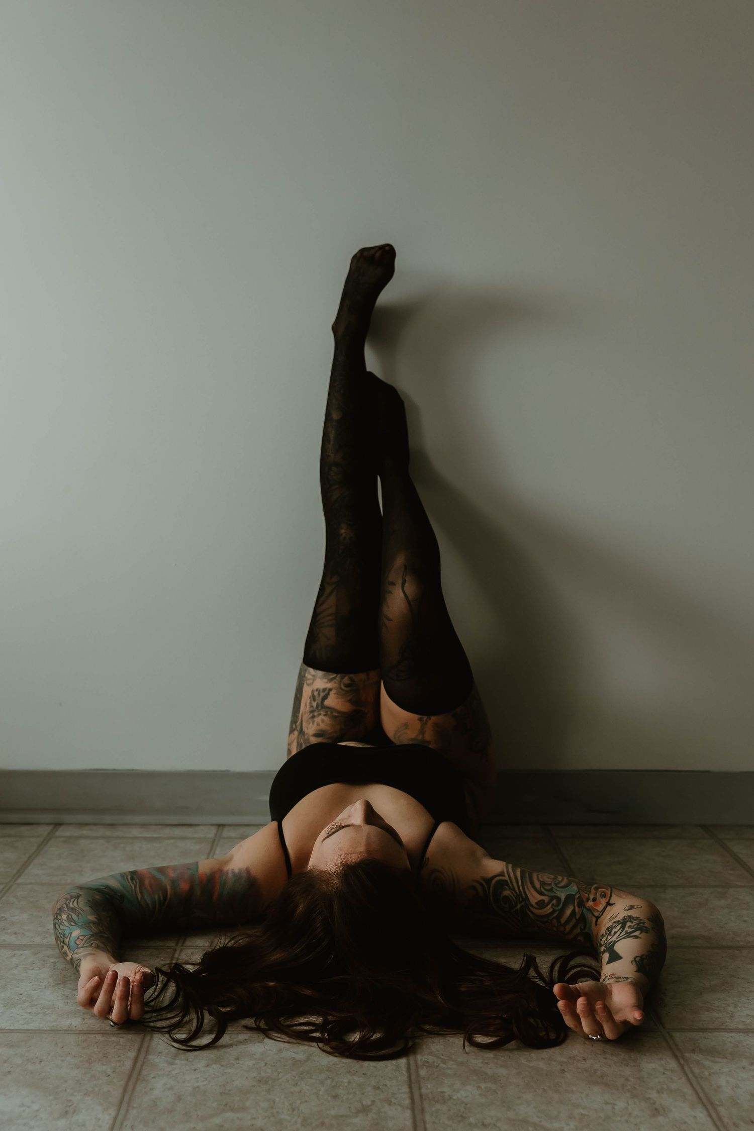 Figure in black lingerie and stockings reclining on floor with dark hair splayed out against white walls.