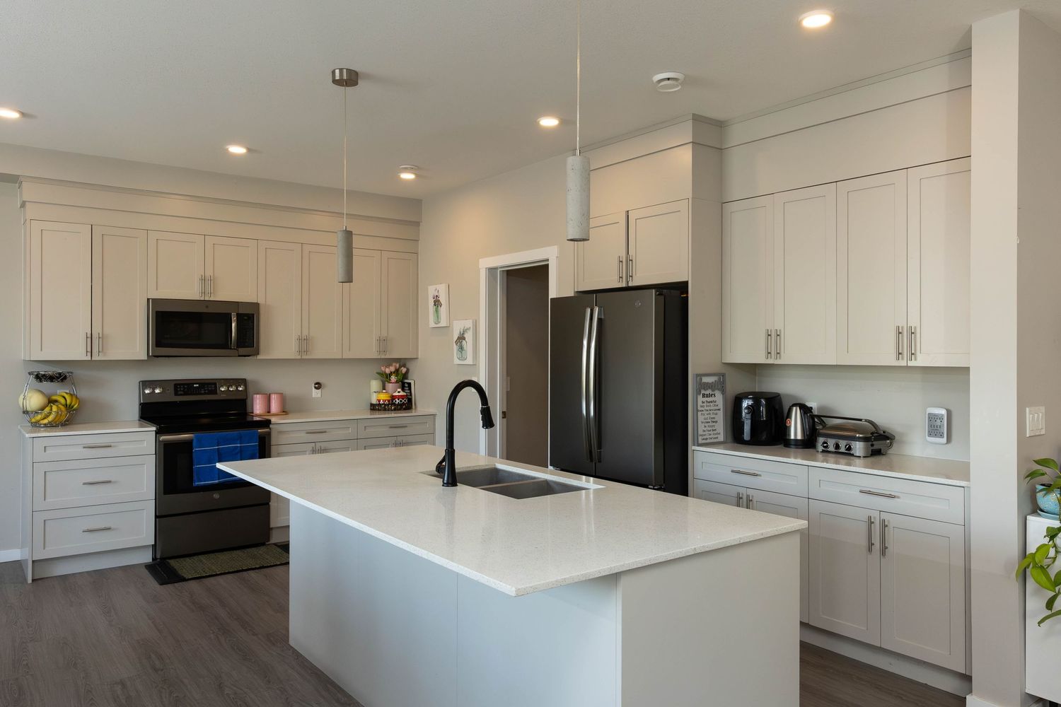 Modern white kitchen with quartz island, stainless appliances, dark hardwood floors and recessed lighting.