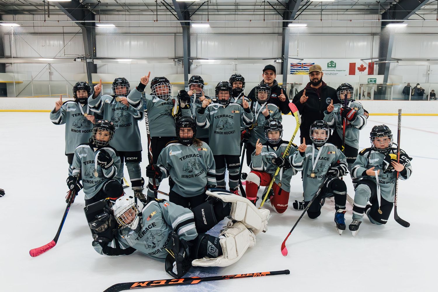 Youth hockey team in matching teal jerseys poses together for a group photo on the ice.