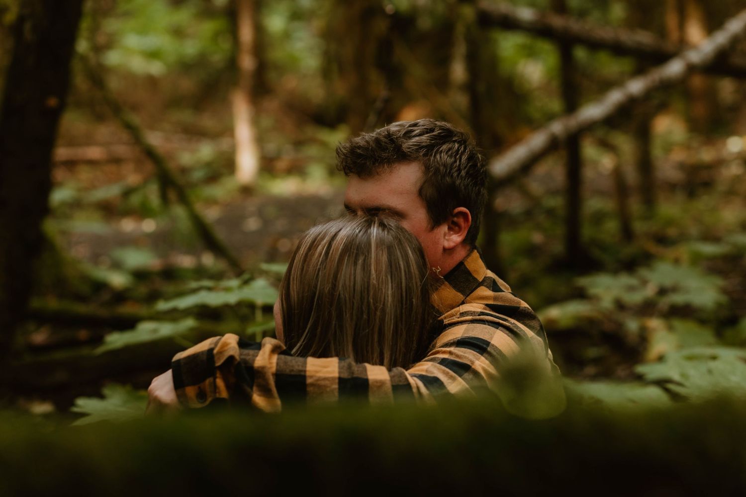 A romantic embrace captured between trees in a mossy forest setting.
