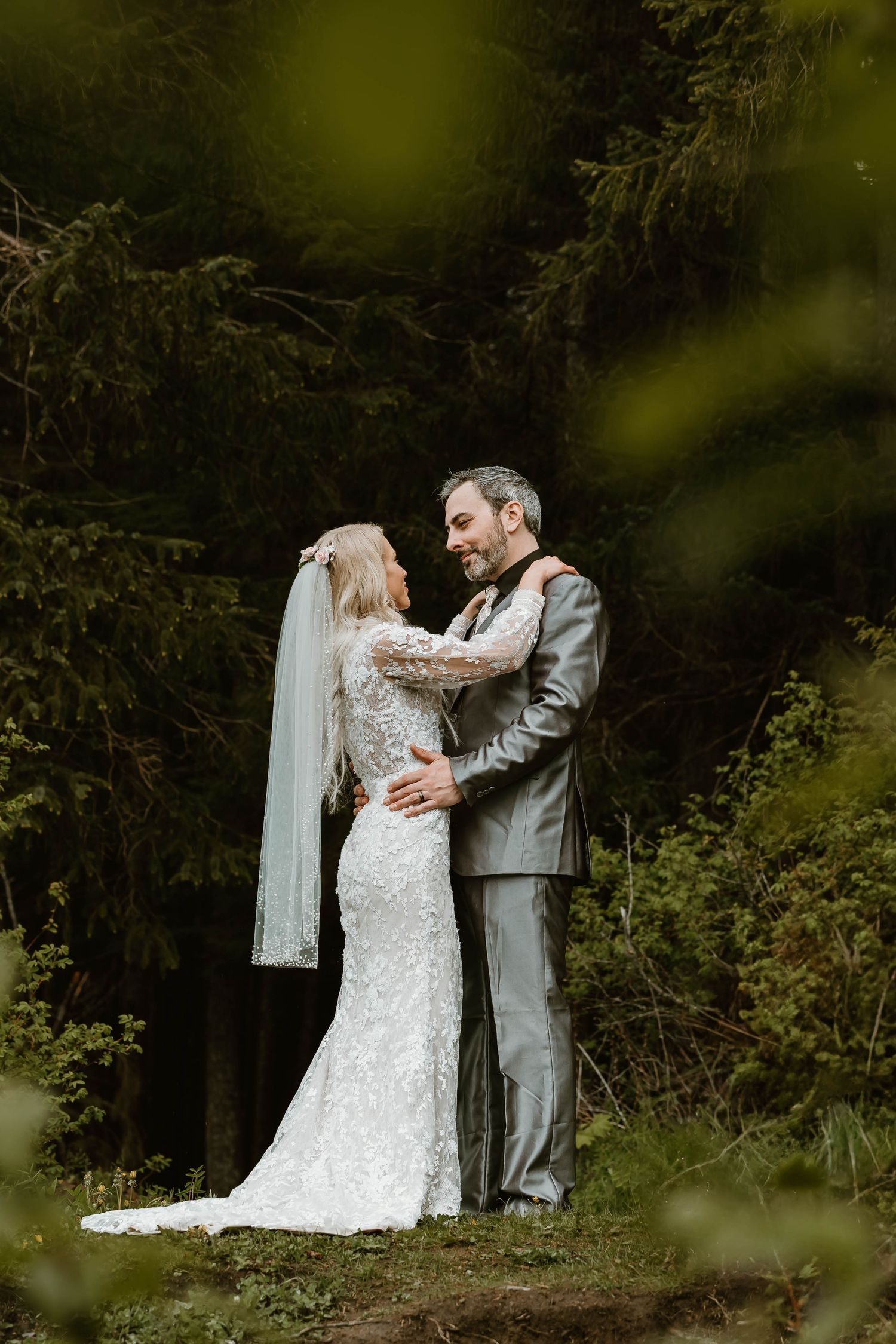 Newlywed couple shares intimate moments during wedding photo session in lush wooded setting.