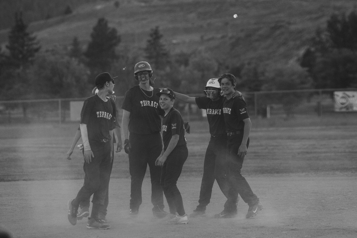 Black and white photo of softball team huddled together on dusty field.