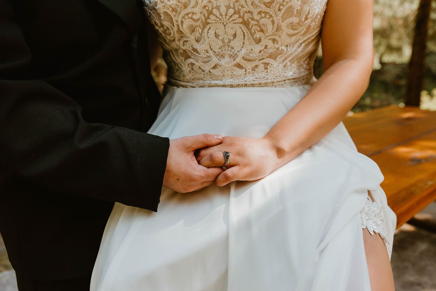 Close up of couple holding hands showing details of white wedding dress and formal suit.