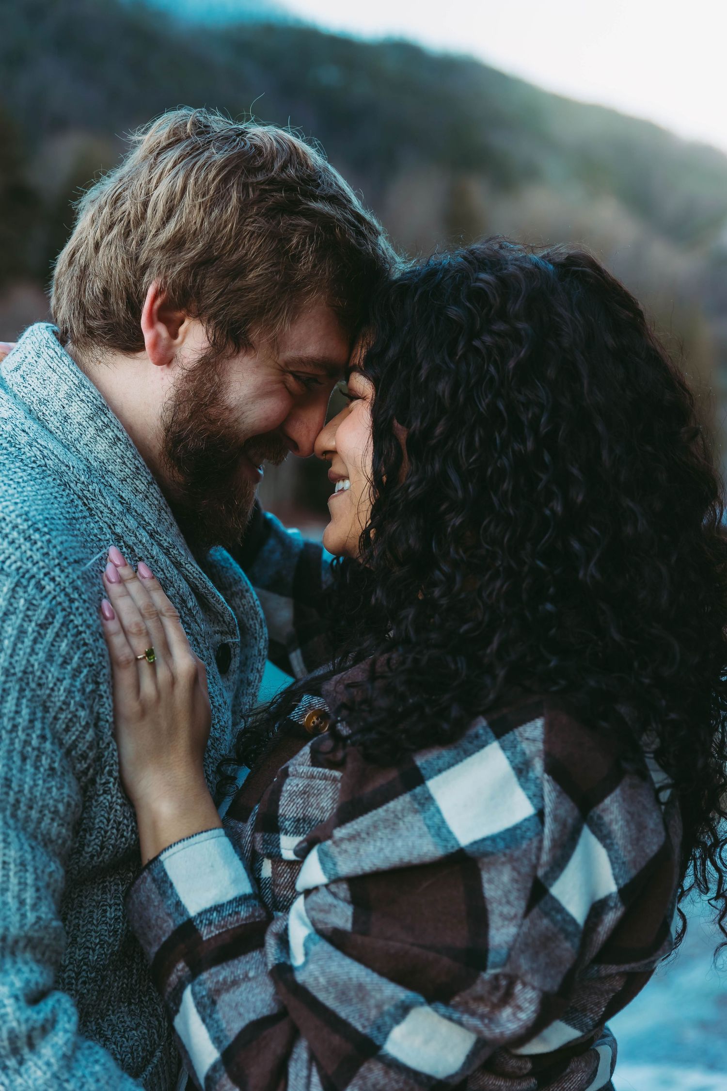 A tender intimate moment shared between a couple wearing cozy sweaters against a mountain backdrop.