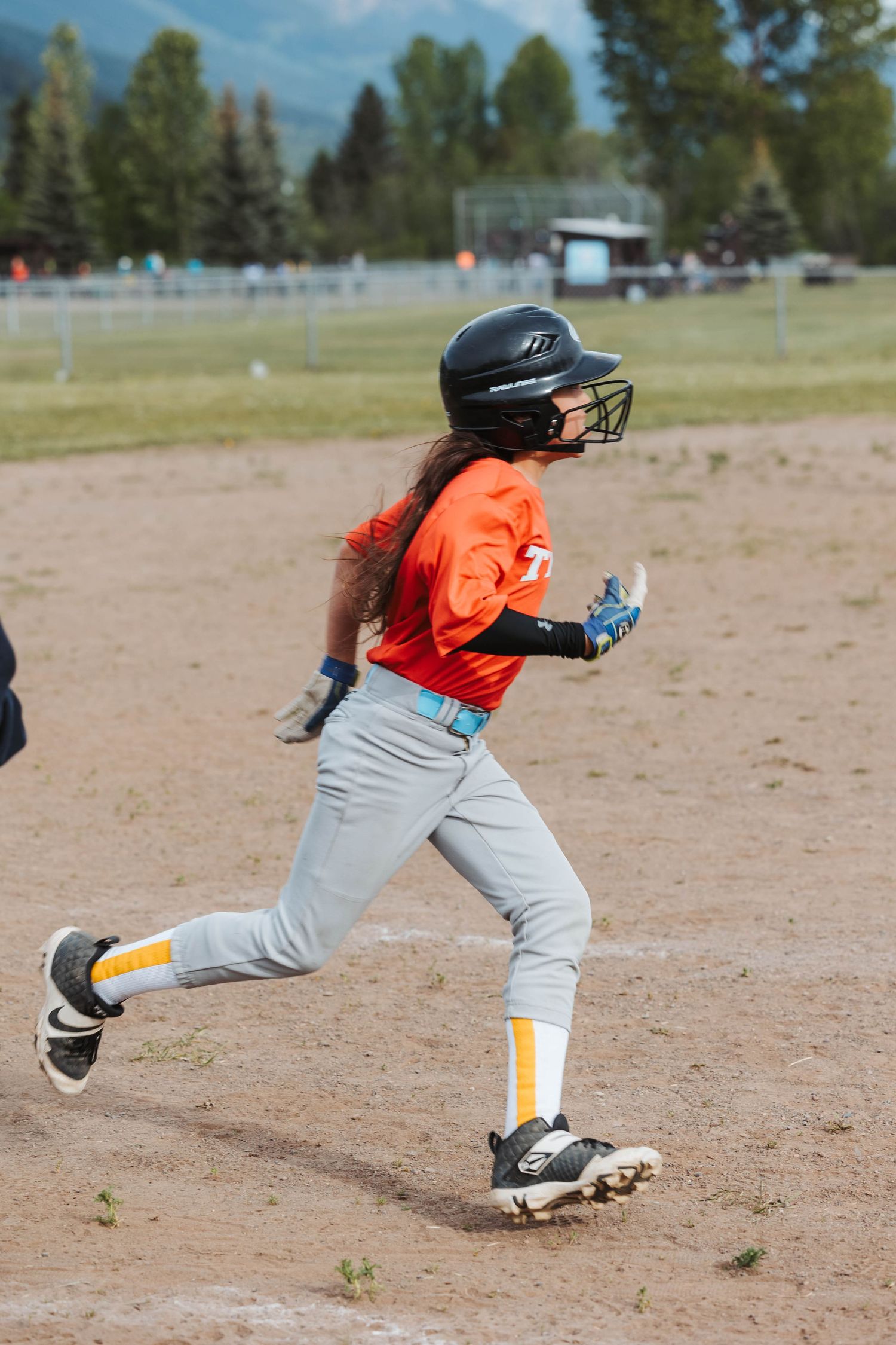 Baseball player in orange jersey and gray pants running on dirt field.