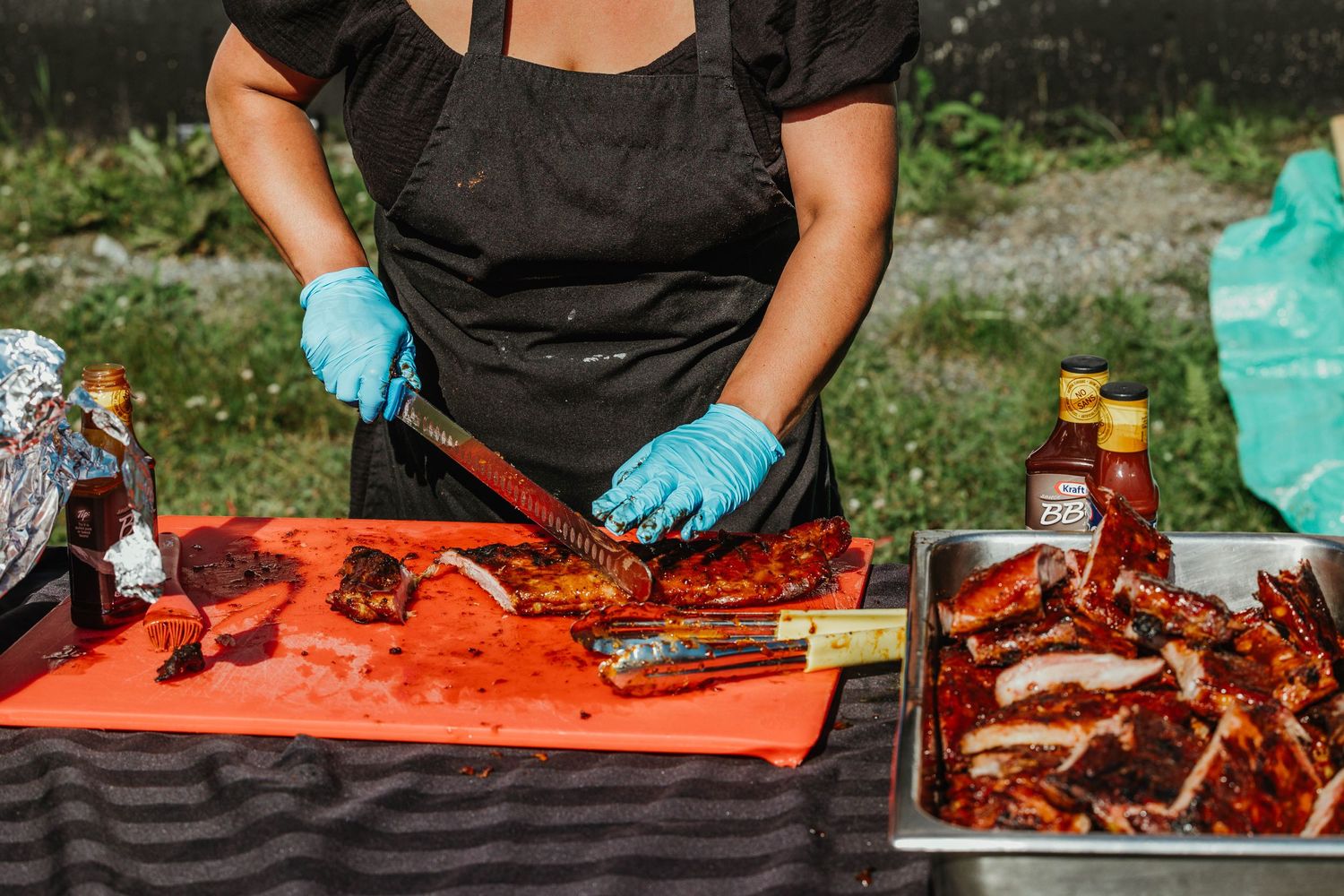 Chef wearing black and blue gloves preparing meat on red cutting board.