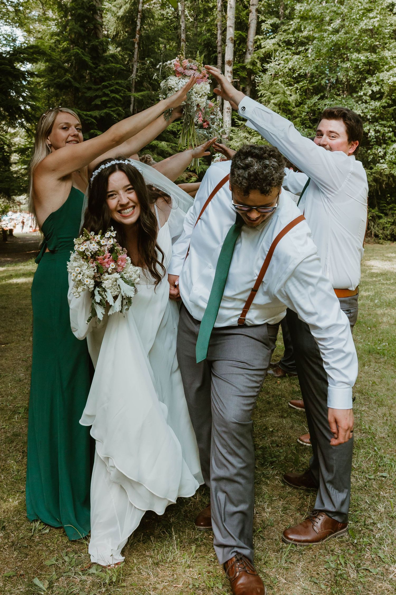 Wedding party celebrating with arms raised forming an arch outdoors.