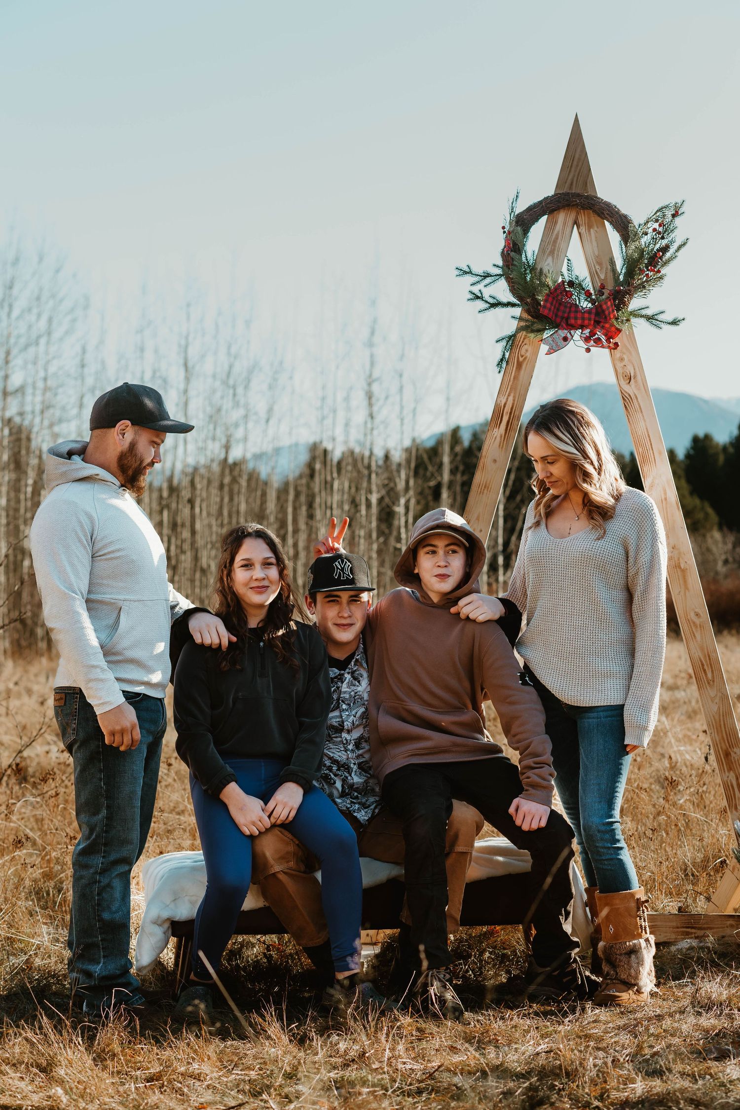 A family group poses together by a wooden triangle structure in a winter field.