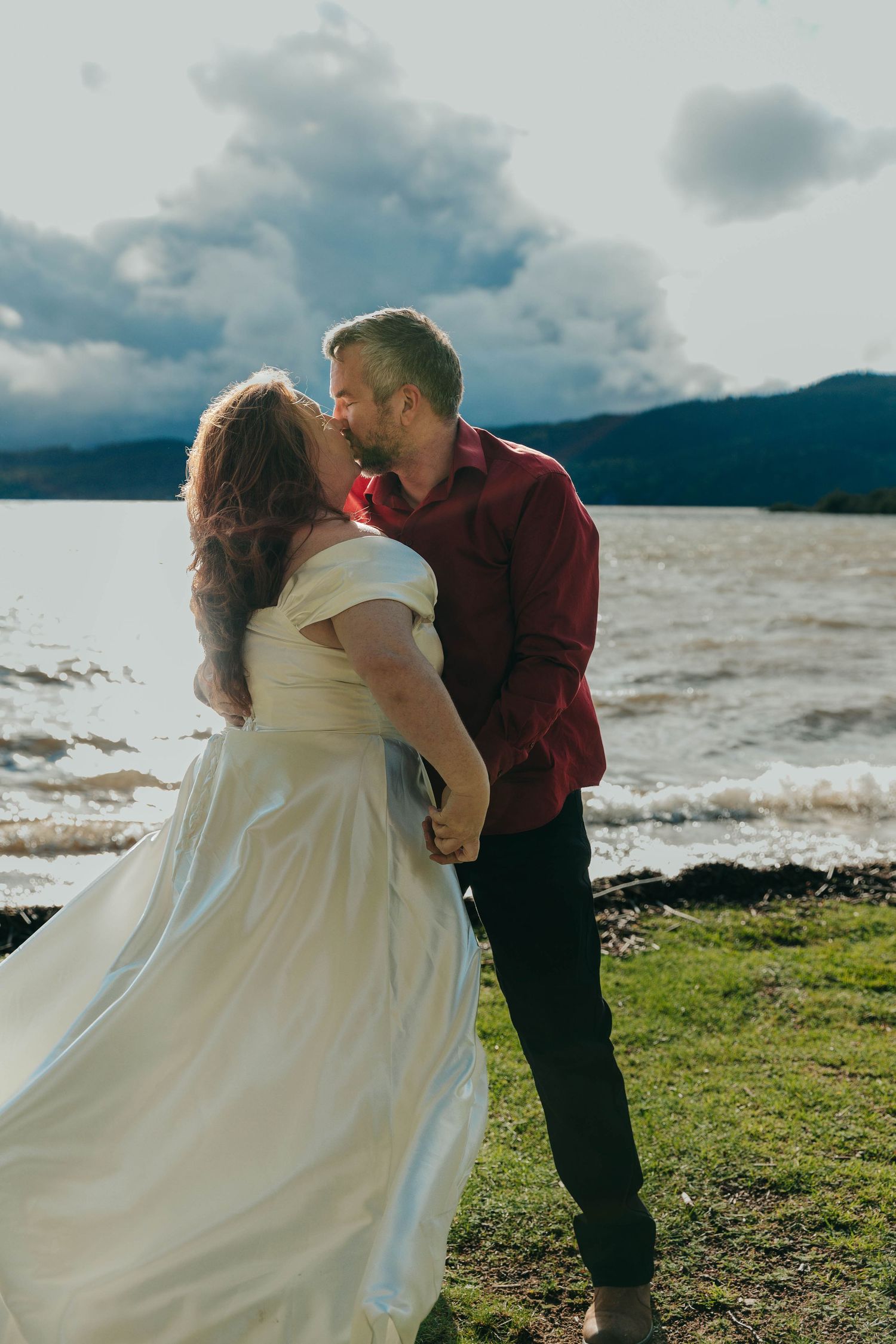 A romantic waterfront moment with mountains and dramatic clouds in the background.
