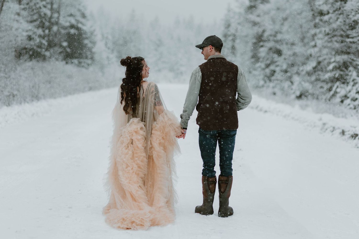 A couple walking hand in hand through a snowy forest path.