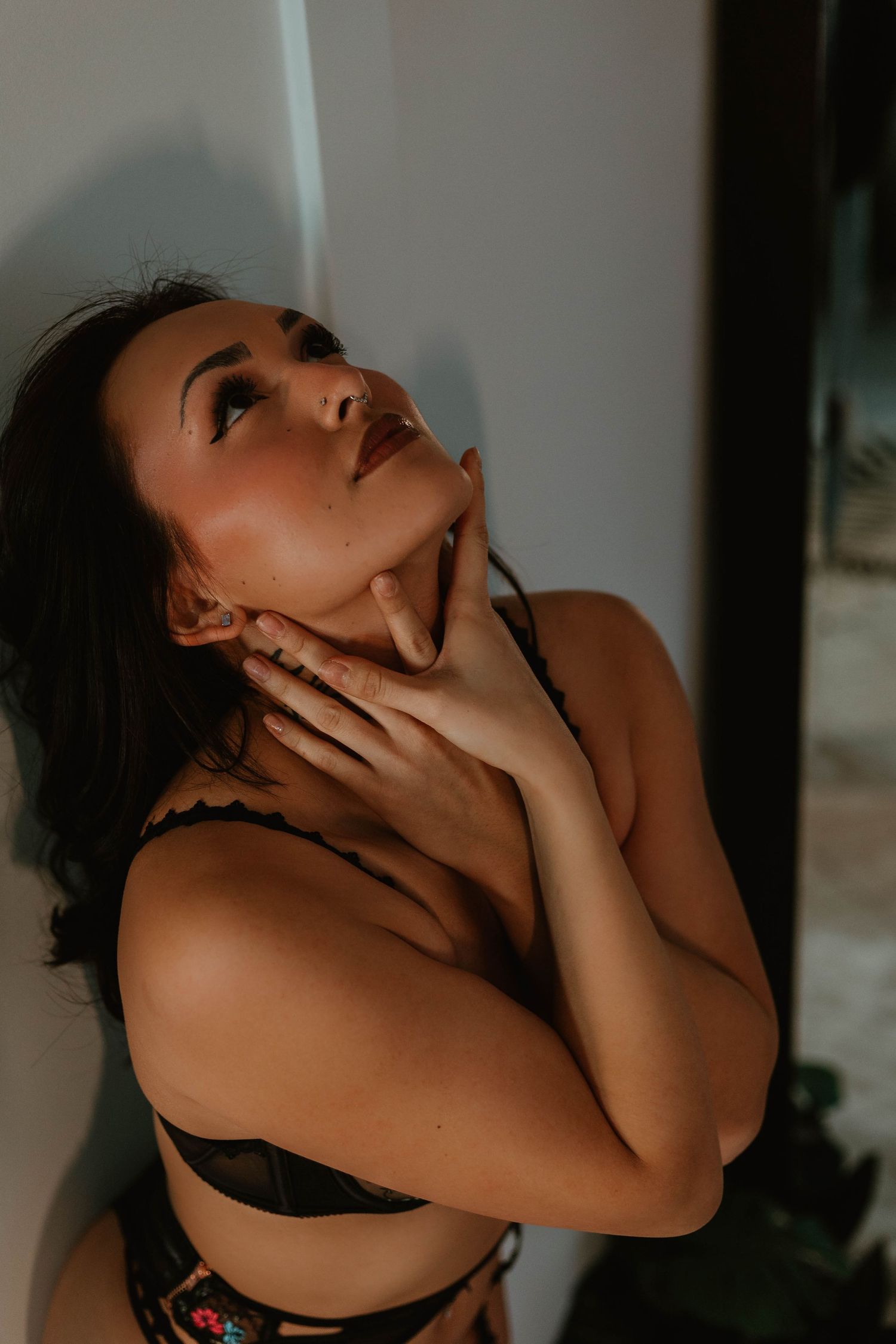 Artistic portrait of person in moody lighting holding their neck and looking upward in contemplation.
