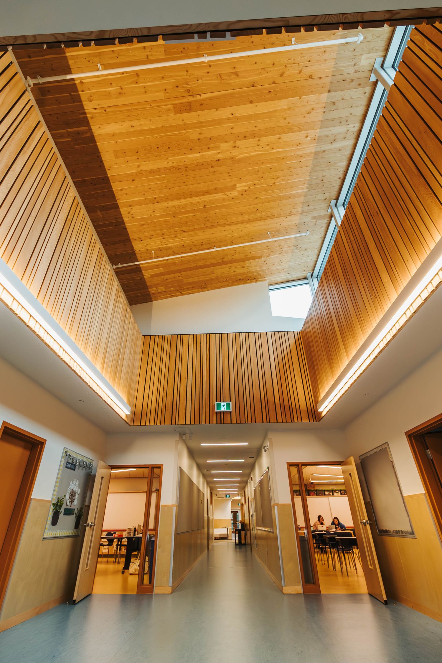 Contemporary institutional corridor with vaulted wooden ceiling and skylight.