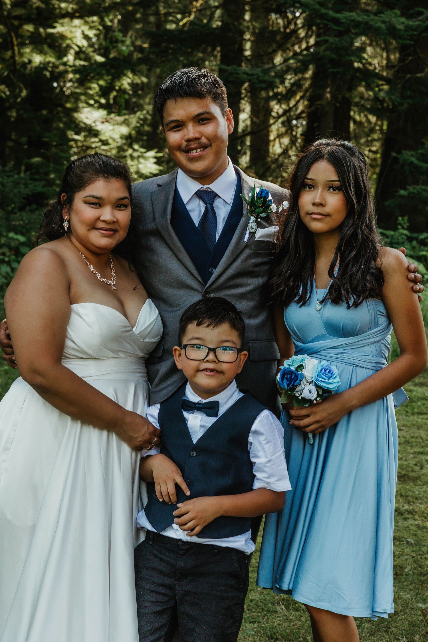 Wedding group portrait in forest with formal attire and matching blue color scheme.