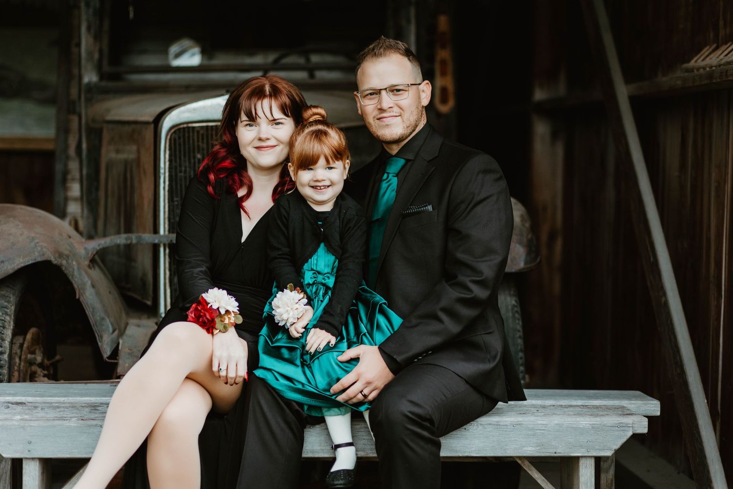 A family in formal black and teal outfits poses together on a vintage truck bench.