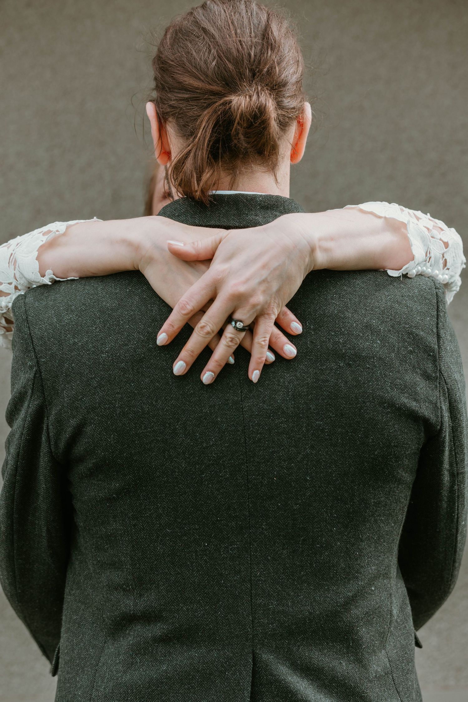Close-up of lace-covered arms embracing groom from behind showing wedding ring.