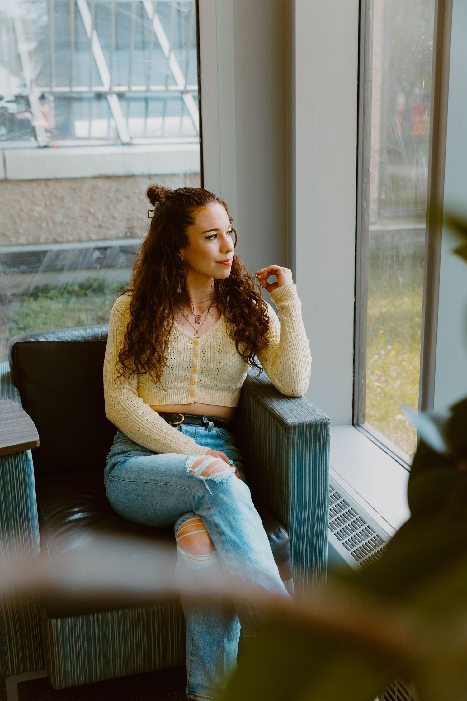 Person in cream sweater gazes thoughtfully out window while relaxing in chair.