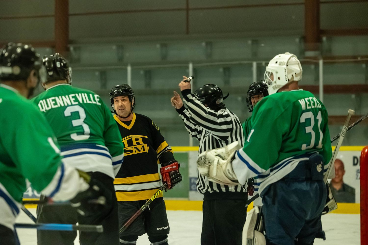 Hockey referee signals during a game between teams wearing green and black uniforms.