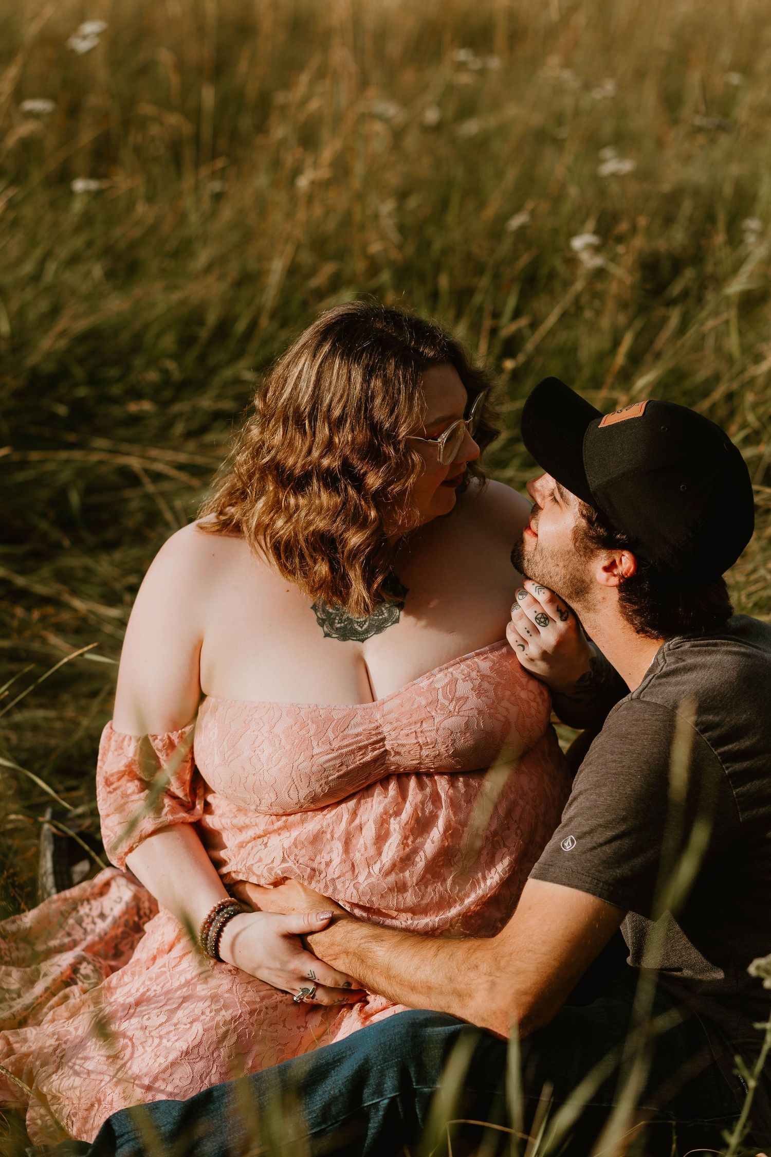 A couple shares an intimate moment while sitting in tall grass at sunset.