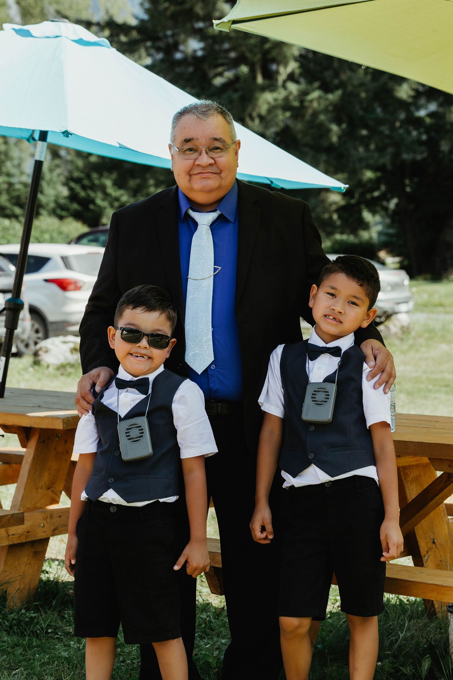 Three generations in formal attire pose together under patio umbrellas at an outdoor event.
