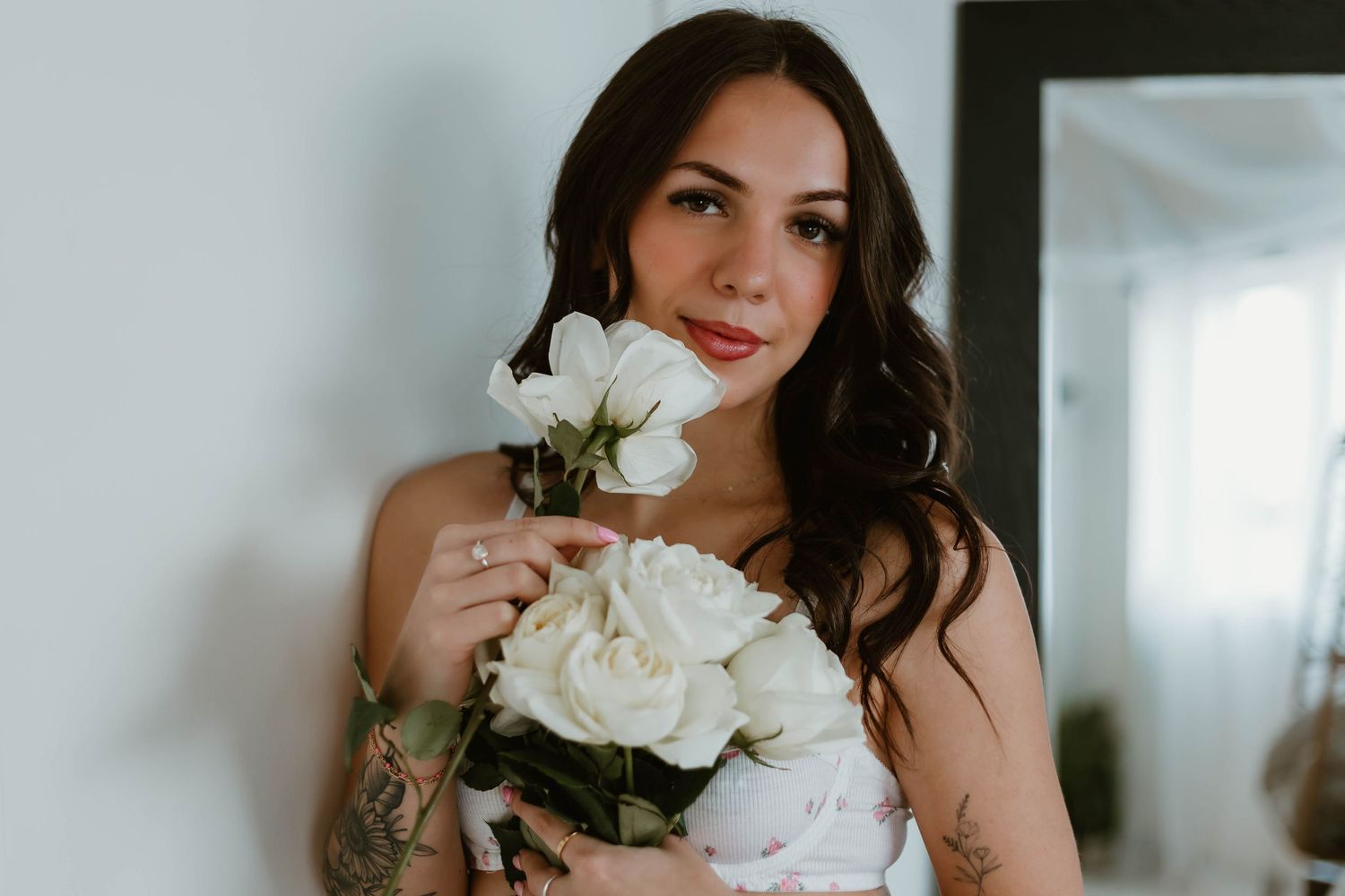 Portrait with white roses against white wall showing delicate romantic styling.