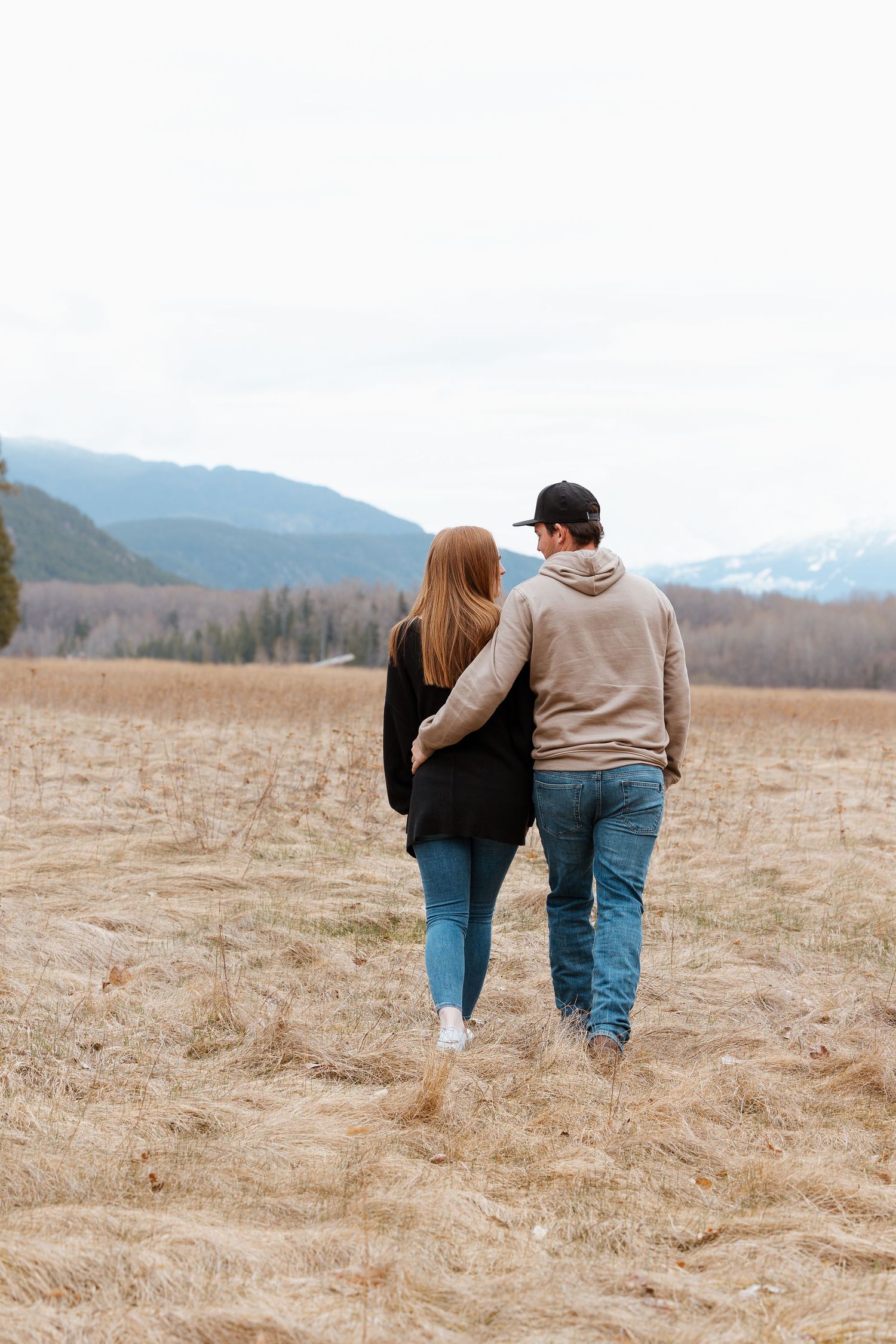 Two people walking together in field with mountain landscape behind them.