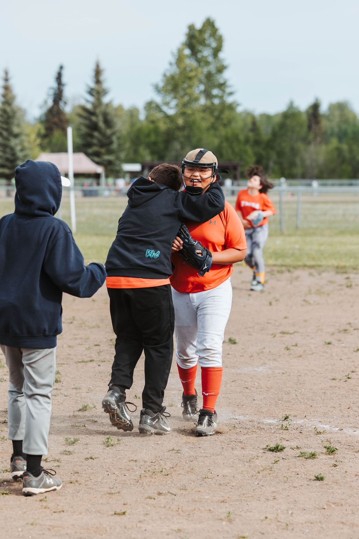 Baseball players and coaches embrace on field after game with mountains in background.