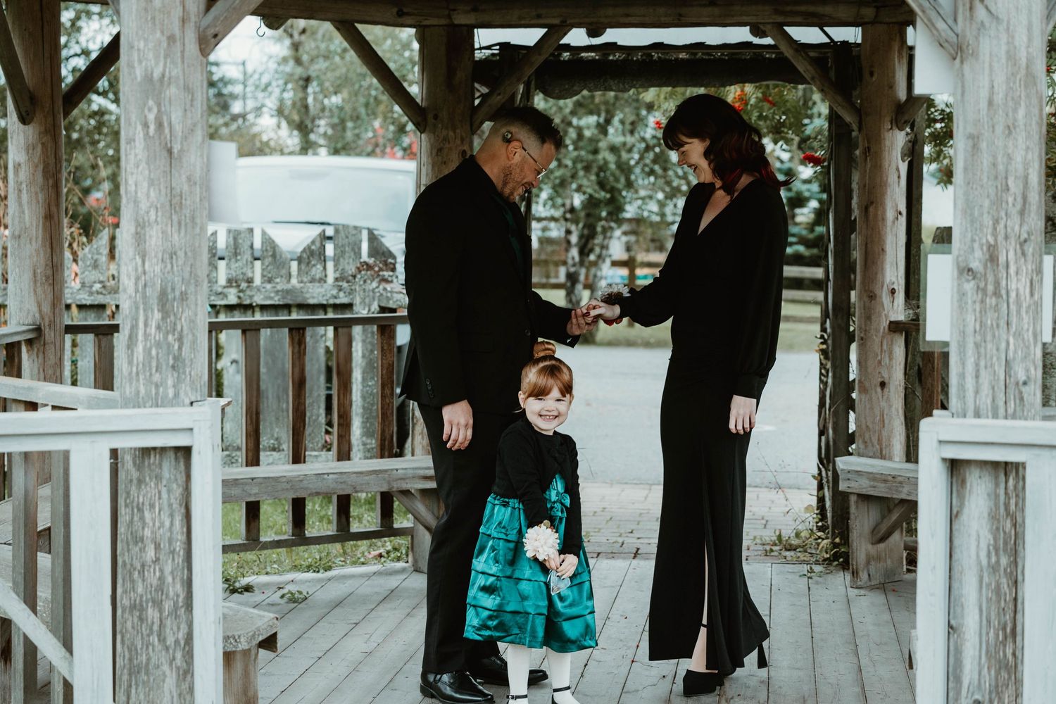 Family in black and teal outfits standing together under wooden gazebo.