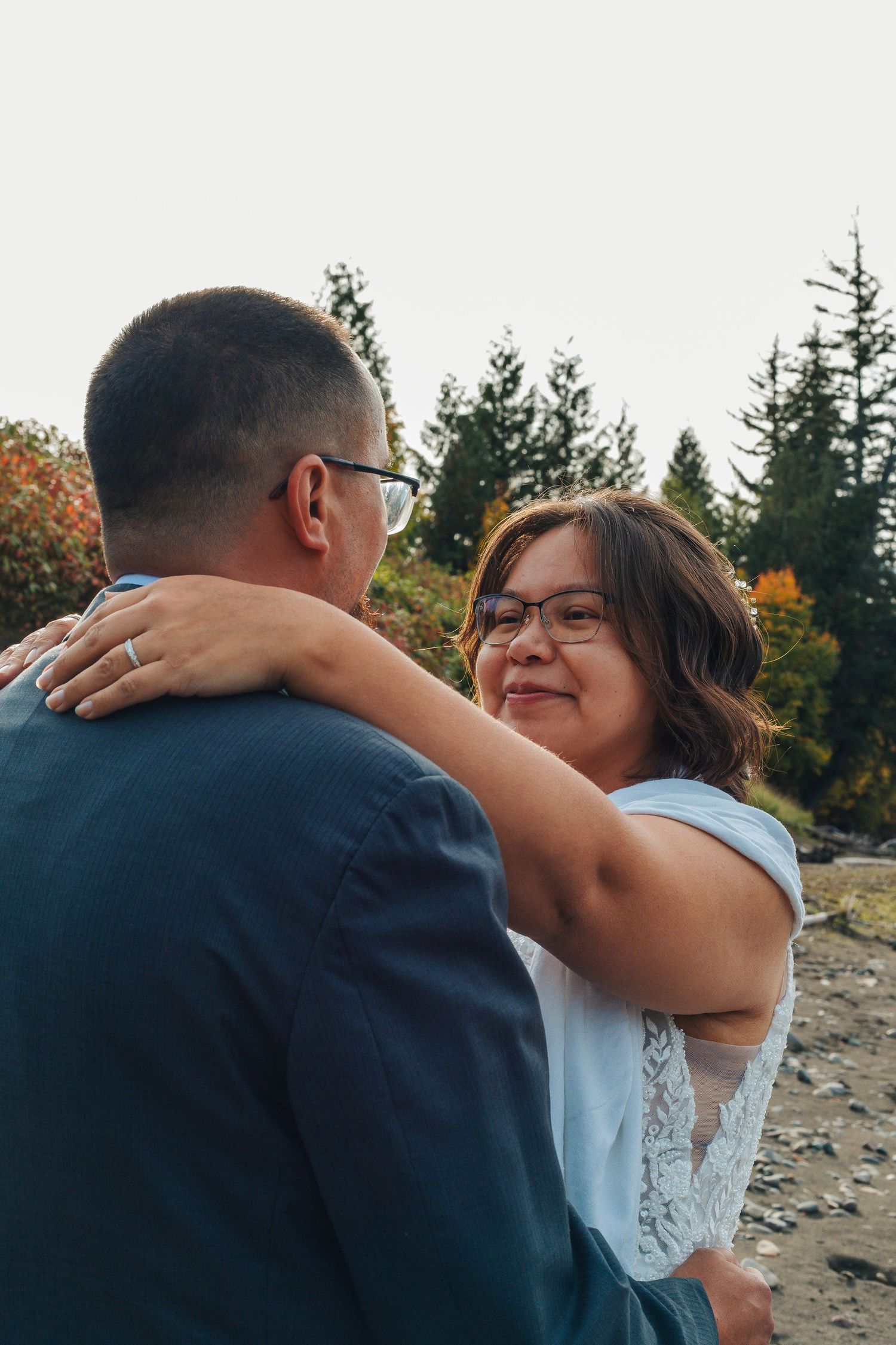 A romantic embrace captured in an outdoor setting with mountains and evergreen trees in the background.
