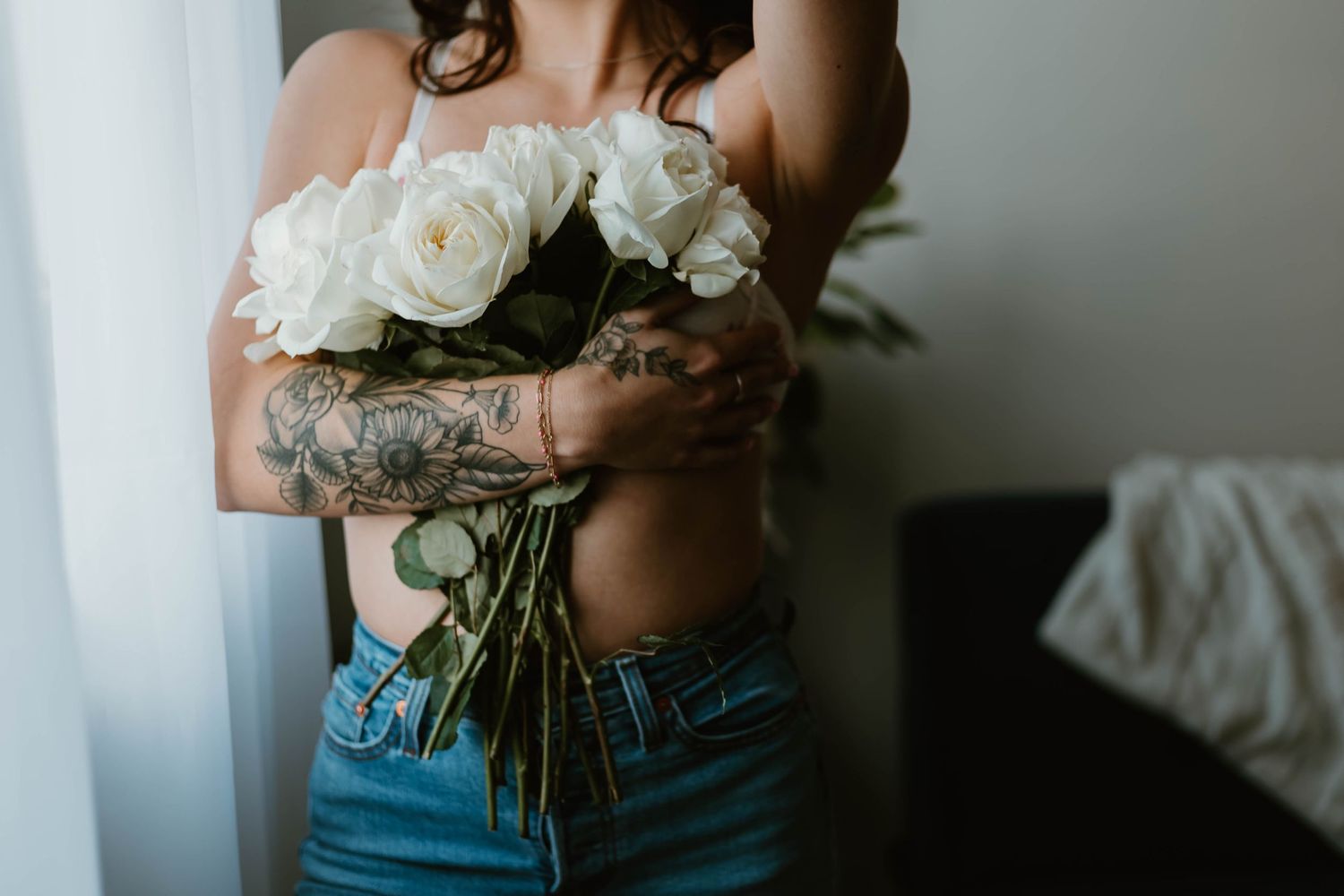 Artistic photo of person holding white roses while wearing denim, showing tattoos.