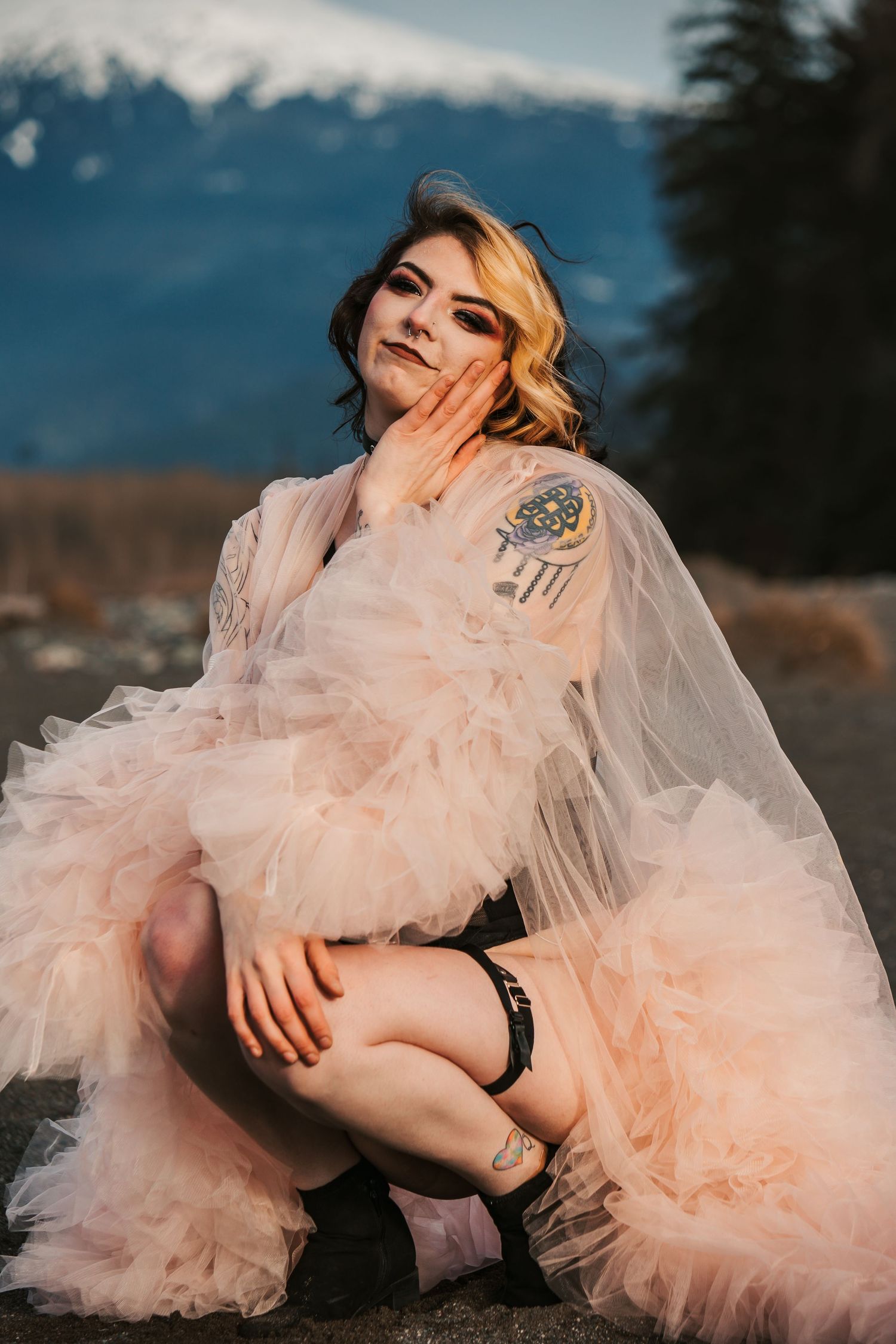 Fashion portrait with flowing peachy tulle dress against mountain landscape.