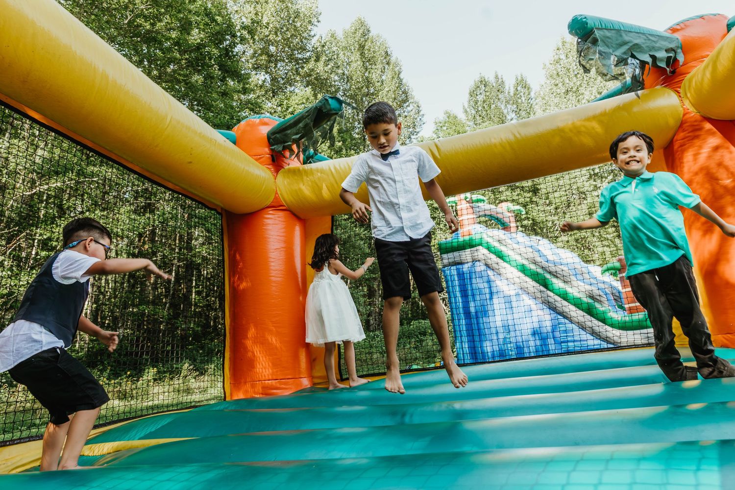 Children and adults jumping and playing on an orange bounce house at an outdoor event.