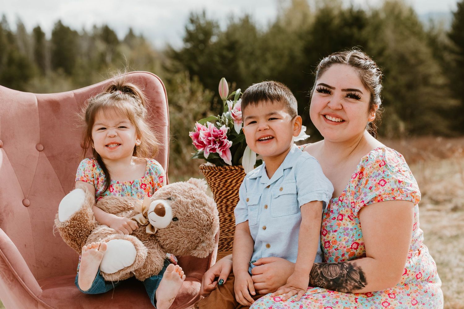 Family portrait on pink chair with floral arrangements and stuffed animals.