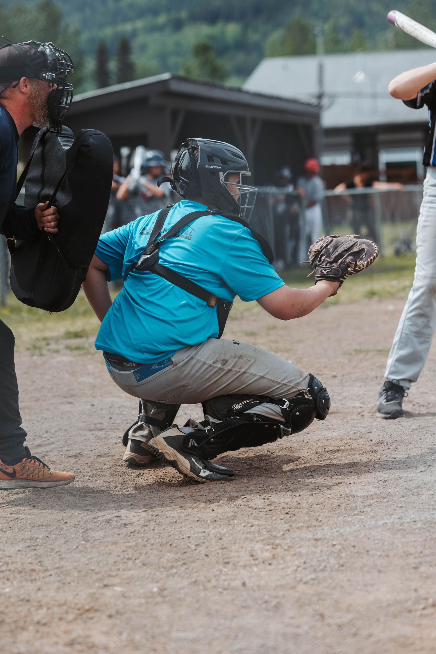 Baseball catcher in a bright blue jersey crouches behind home plate during a game on a dirt field.