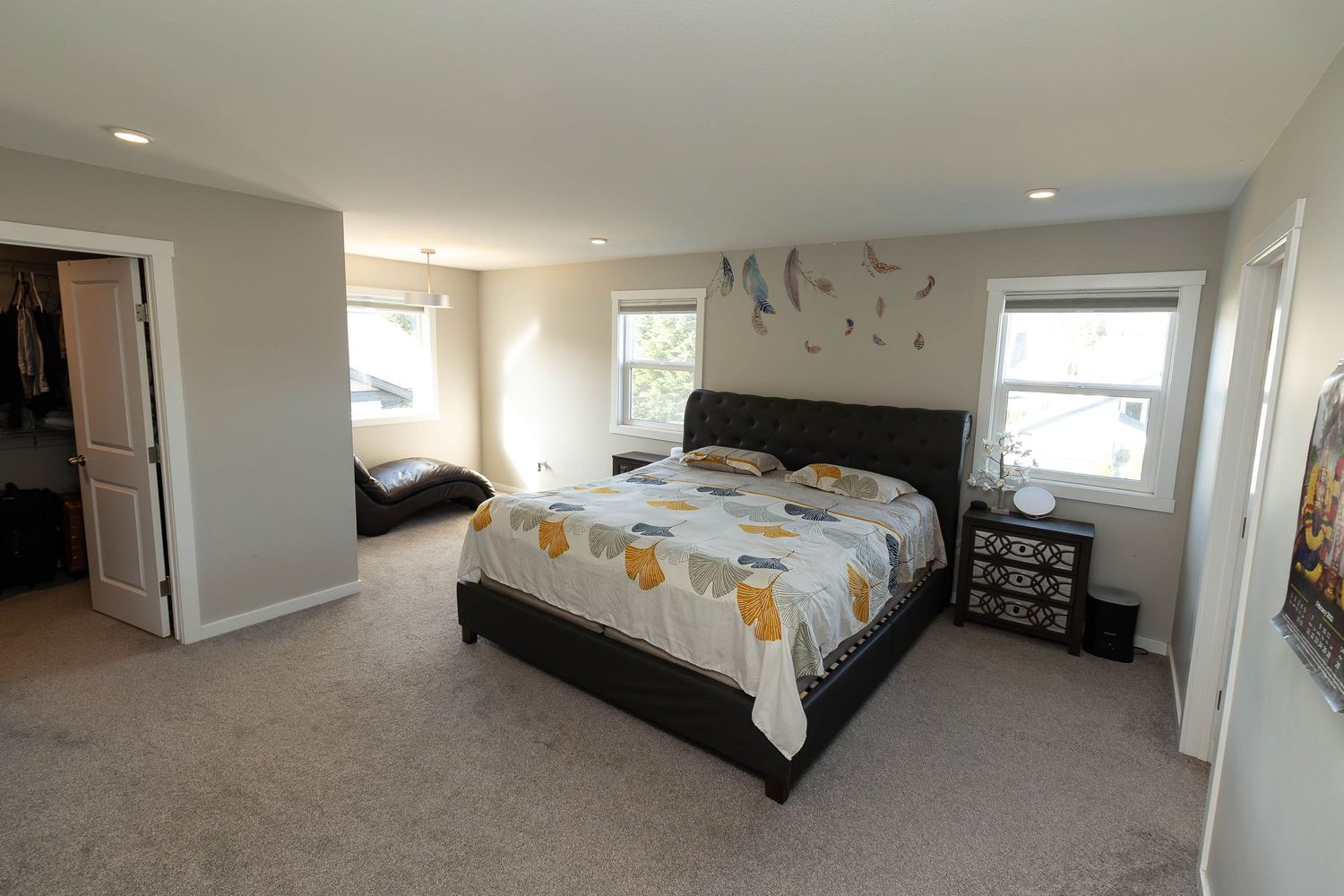 Spacious master bedroom with plush carpeting, king bed with floral bedding, and natural light from multiple windows.