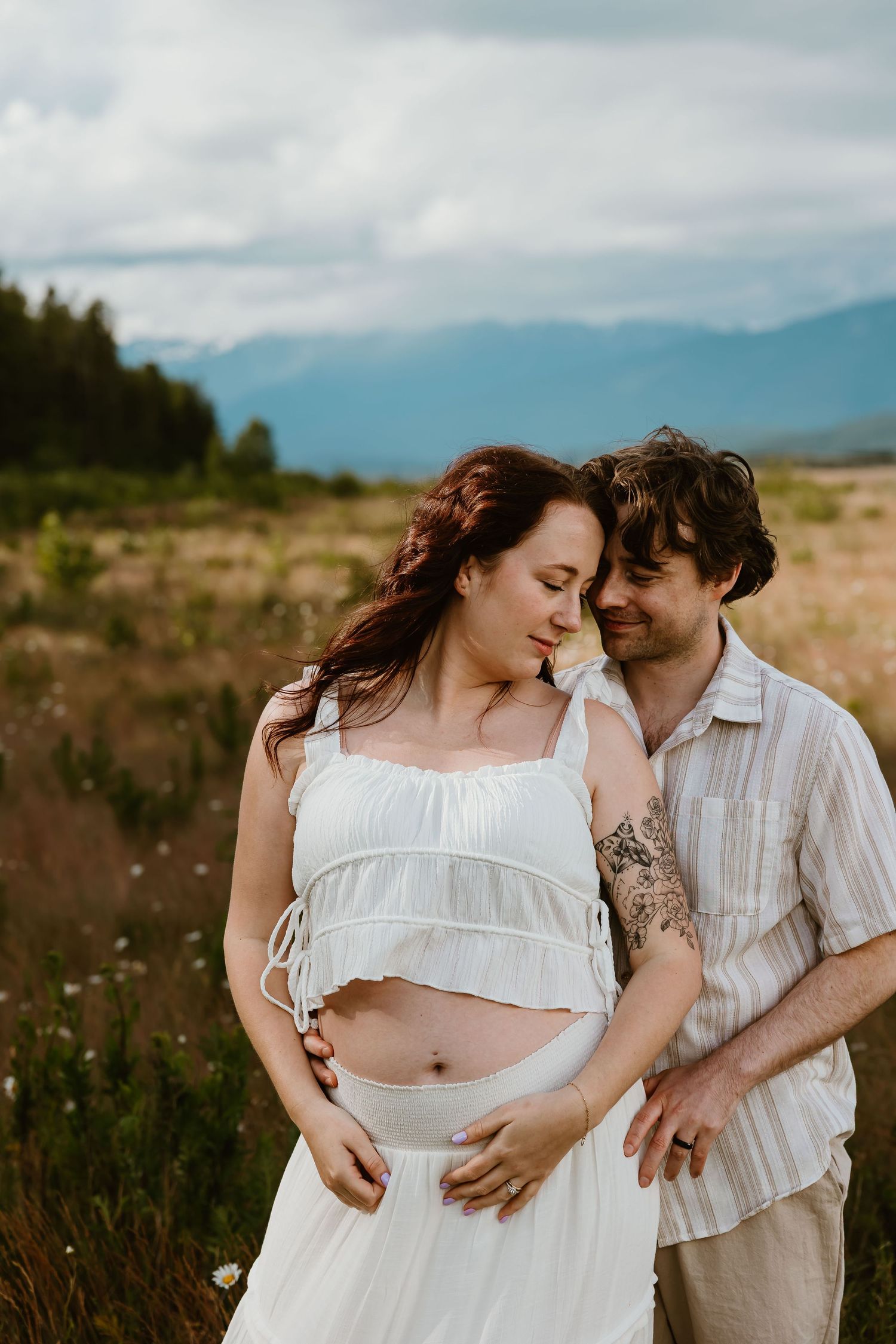 A couple shares intimate moments in a field during a romantic photoshoot with mountains in the background.