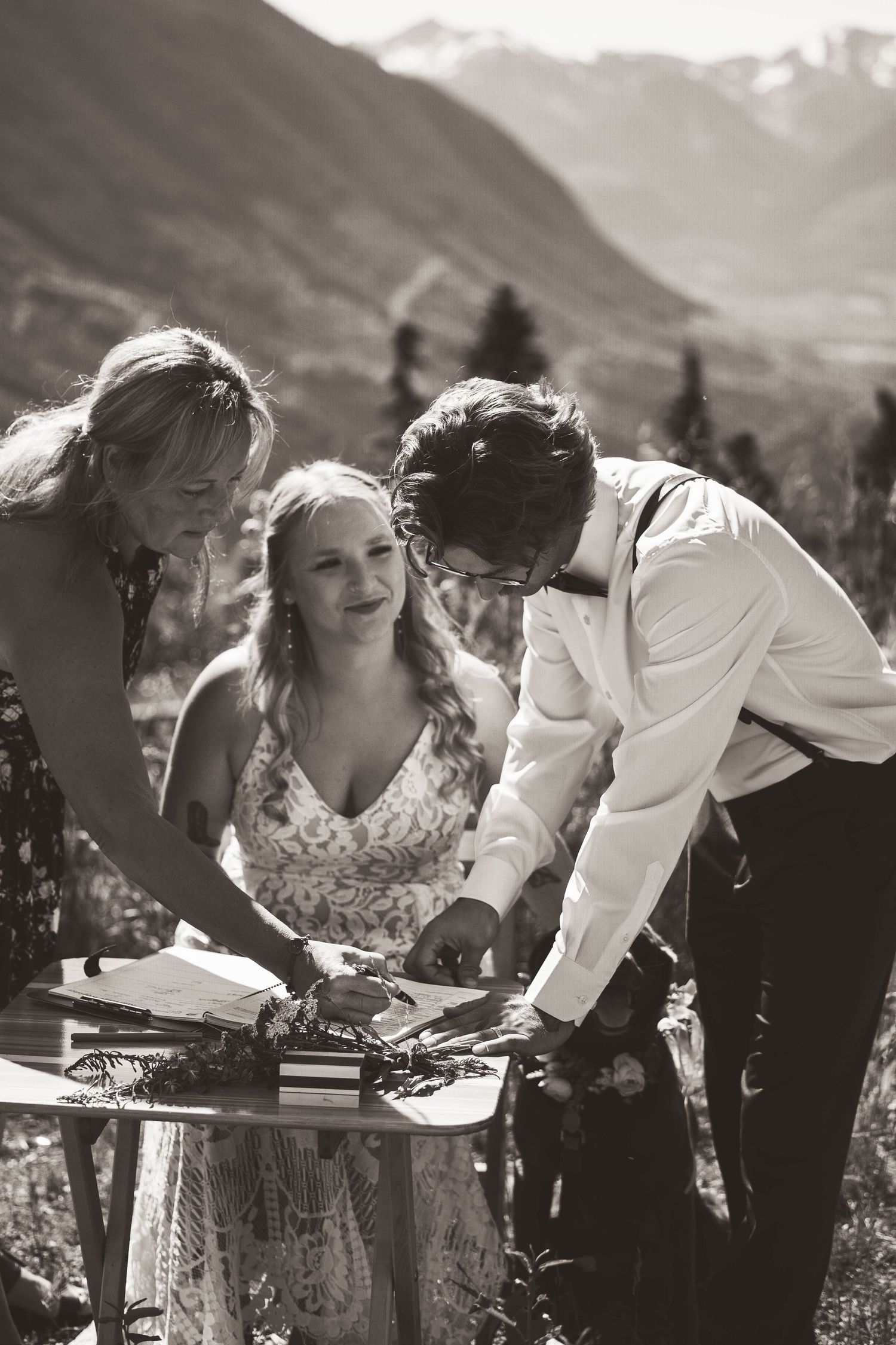 Wedding couple and guest sign documents at a mountain ceremony with dramatic peaks in the background.