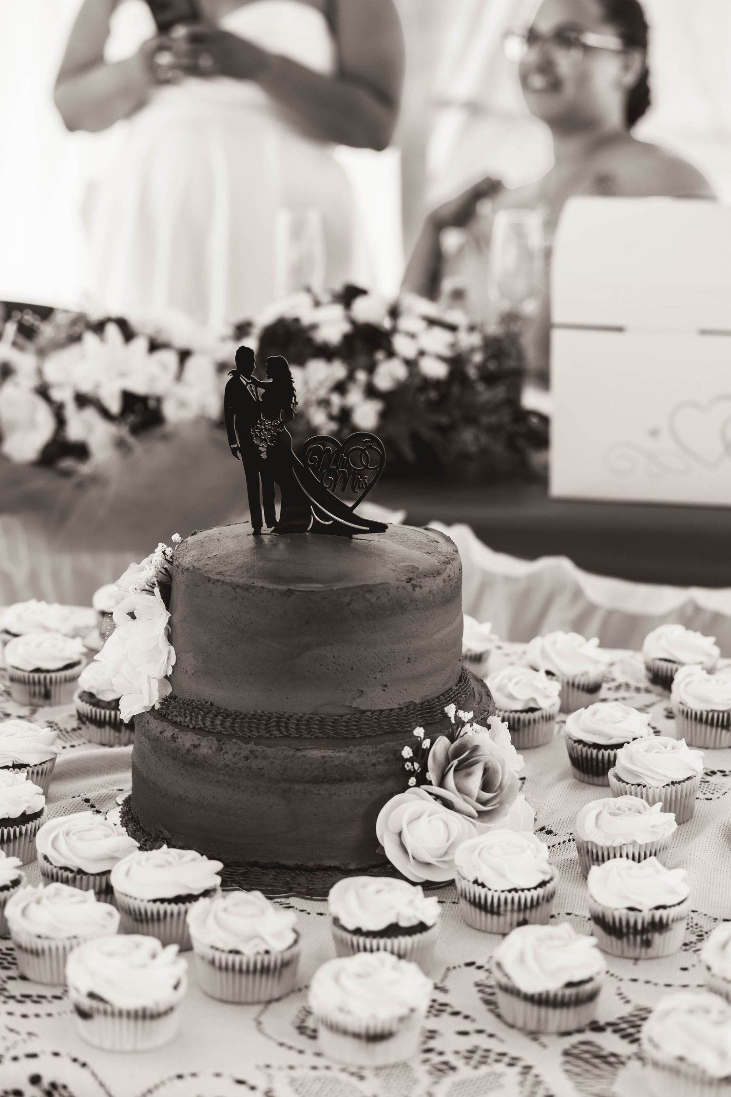 A chocolate wedding cake with white cupcakes and a silhouette cake topper.
