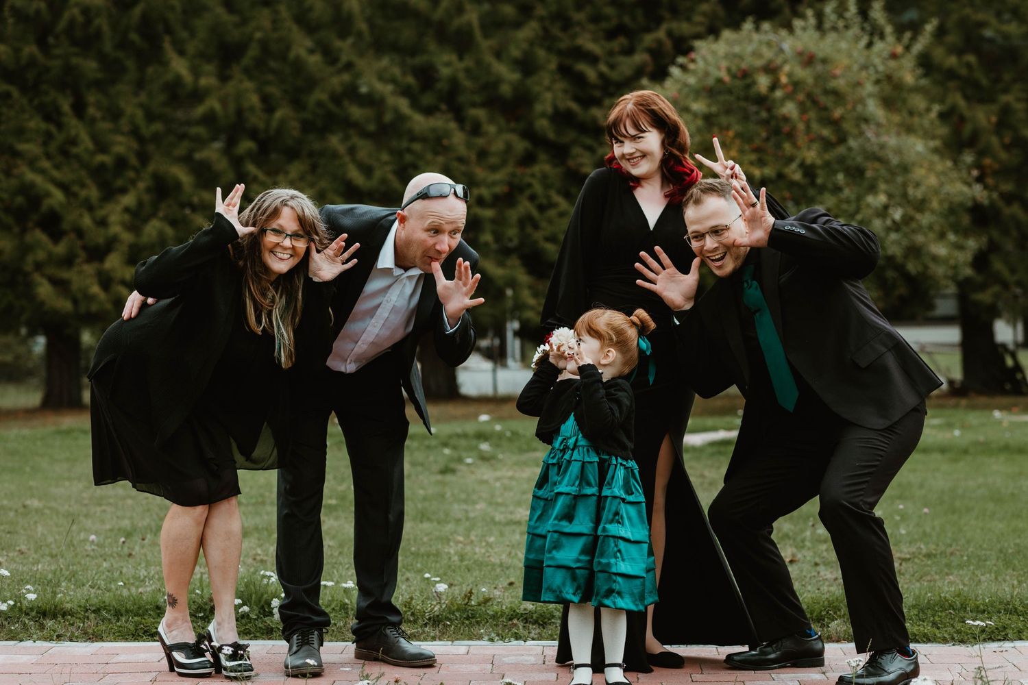 A playful group photo session showing people in black attire making silly poses outdoors.