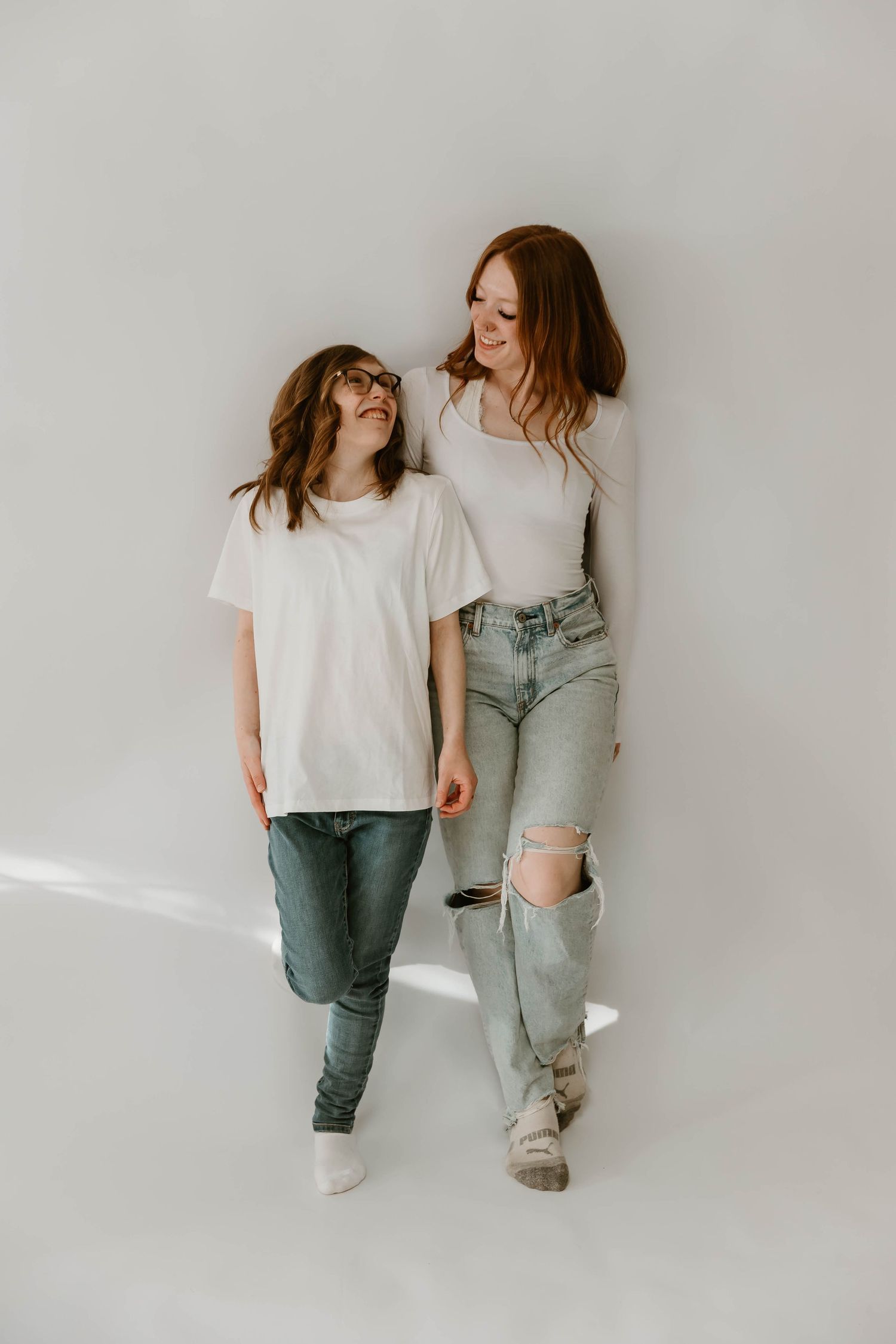Two people in casual denim outfits share a joyful moment against a white backdrop in a minimalist studio setting.