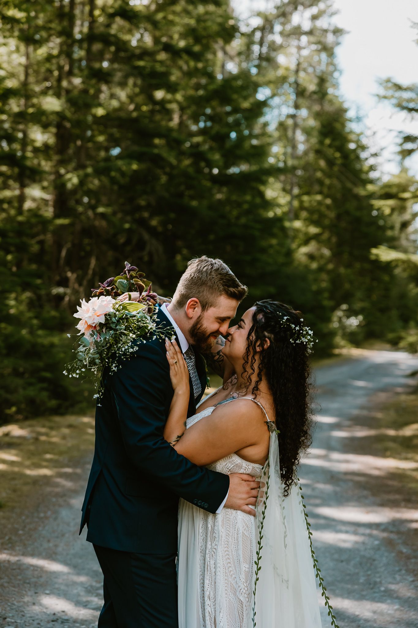 A couple shares a romantic moment on a wooded forest path during their wedding day celebration.
