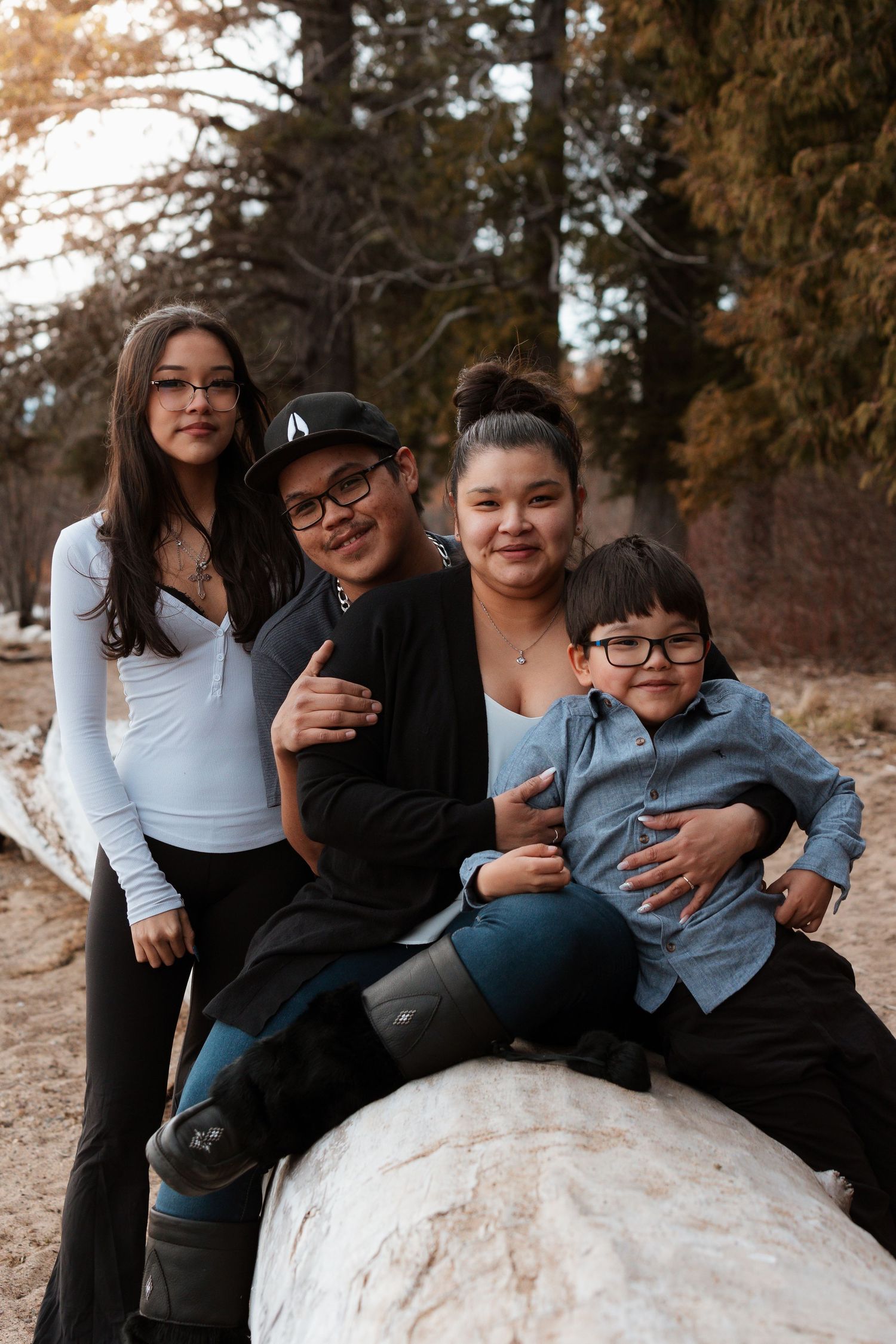 Family sits together on a fallen log during an outdoor photography session.