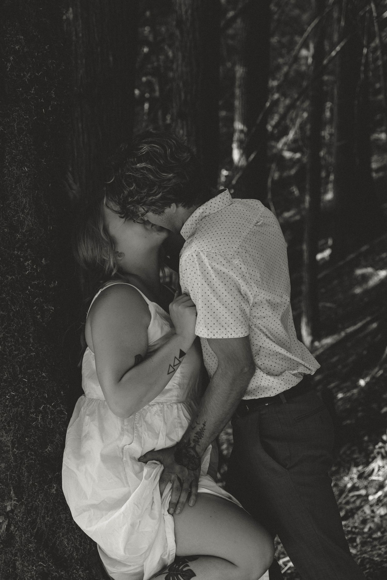 A romantic black and white photo of a couple sharing an intimate moment in a forest setting.