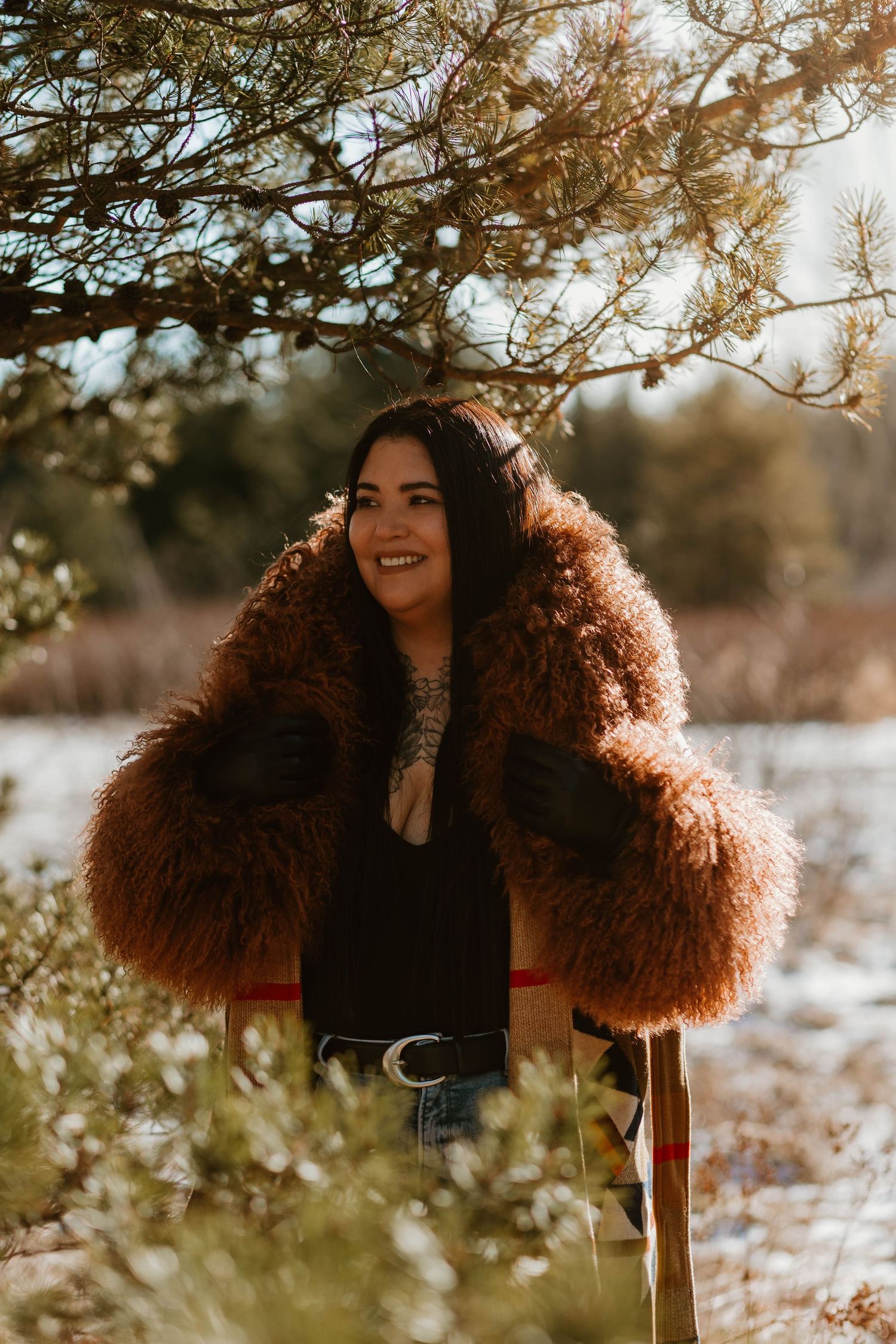 Person wearing vintage-style furry brown coat poses under winter tree branches.