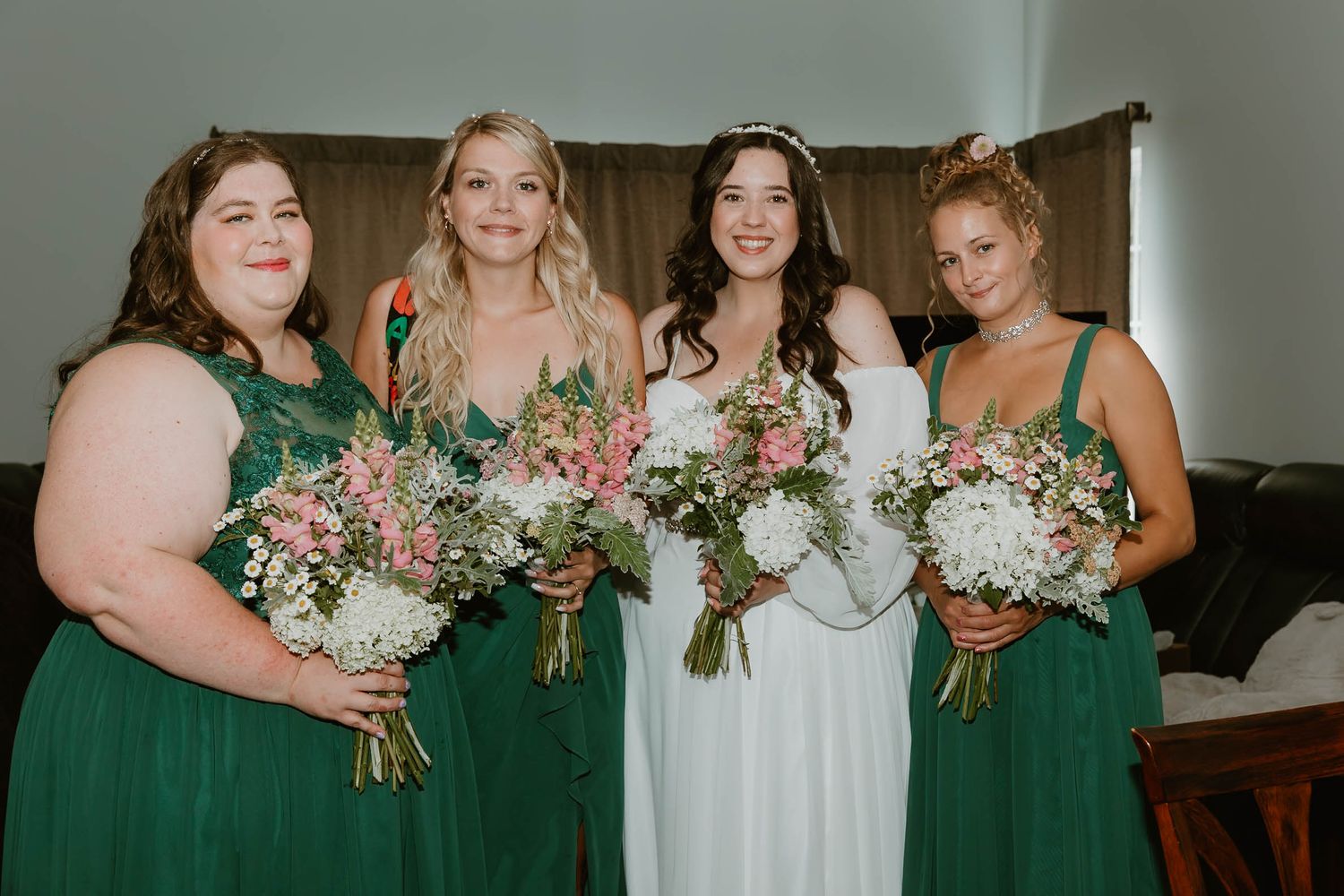 Bridal party in emerald green dresses holds matching floral bouquets.