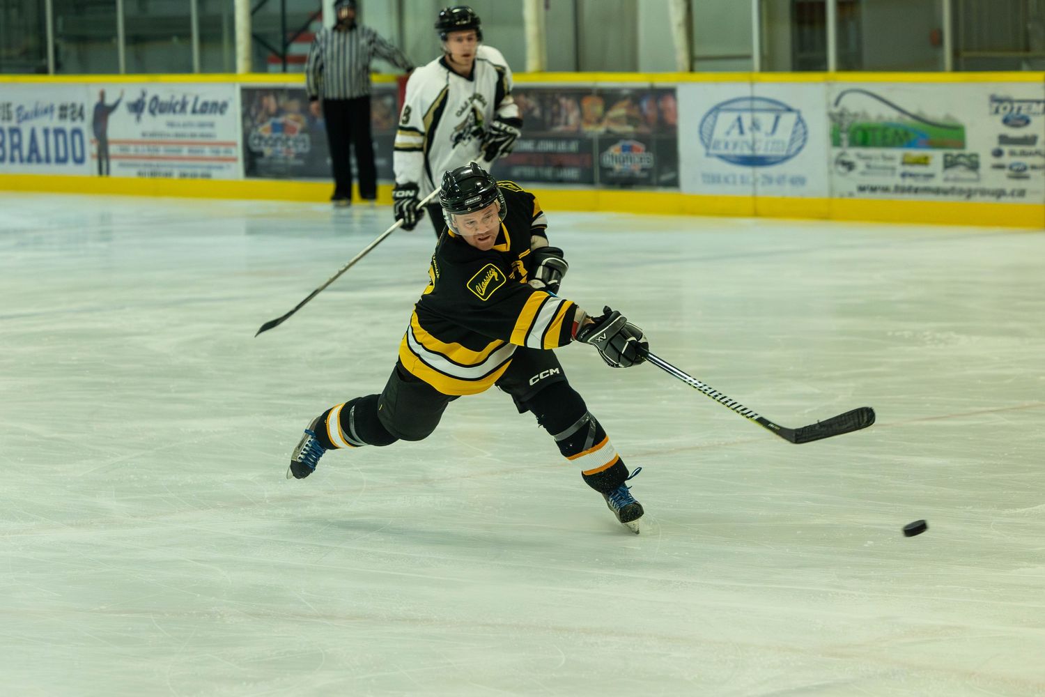 Hockey player in black and yellow uniform takes a shot while skating on the ice.