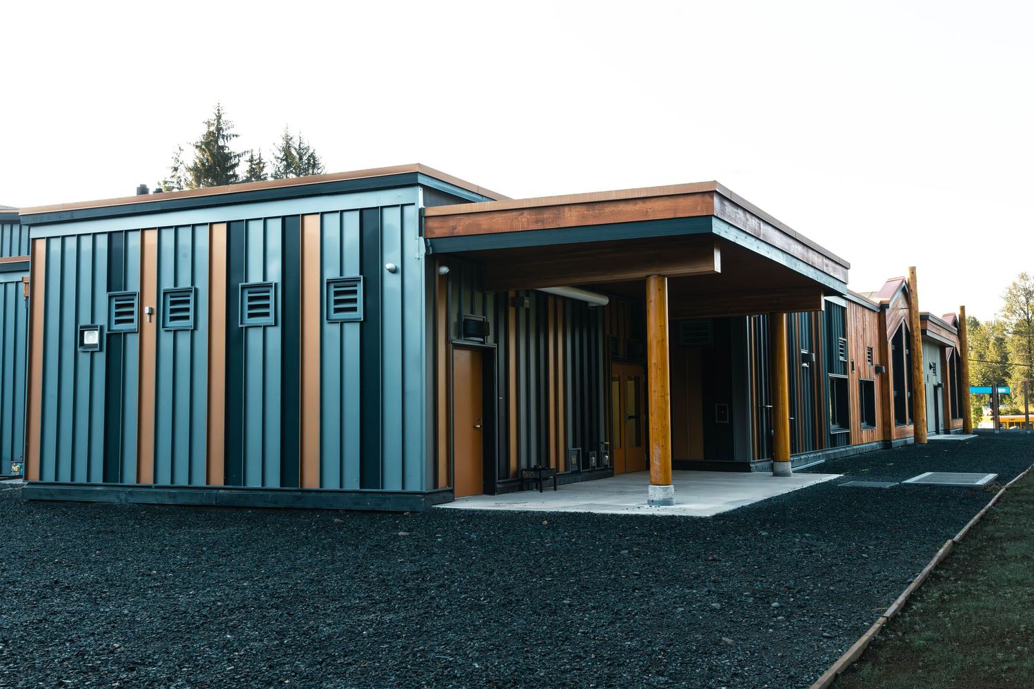 Modern commercial building exterior with teal striped siding and wooden accents features a covered entrance walkway.