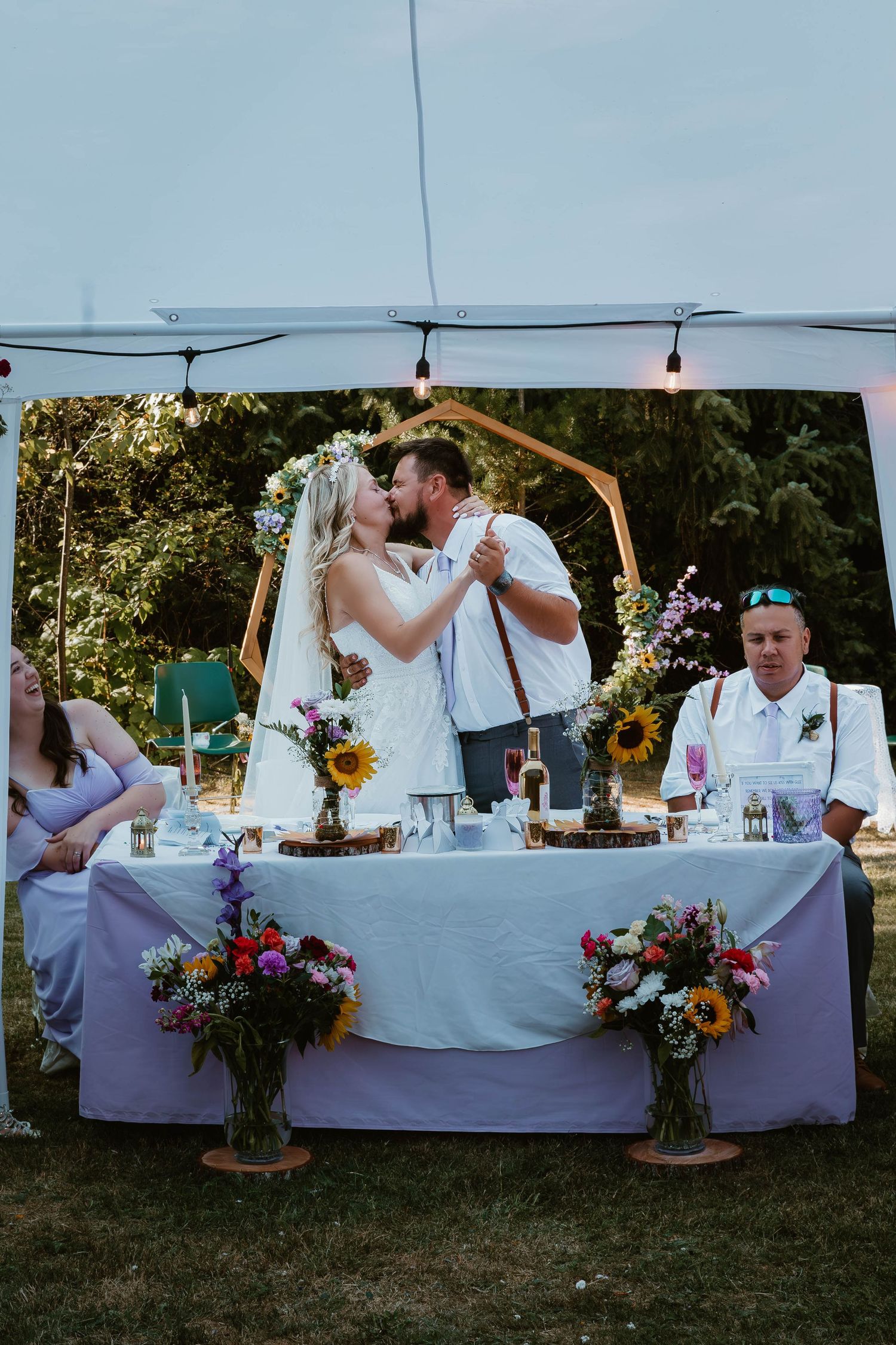 Wedding reception table decorated with flowers as couple shares first dance under string lights.