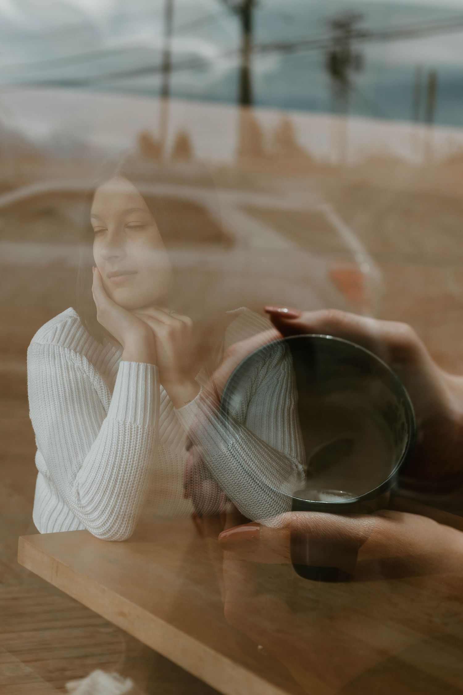 Dreamy window reflection shot of person with coffee cup in warm lighting.