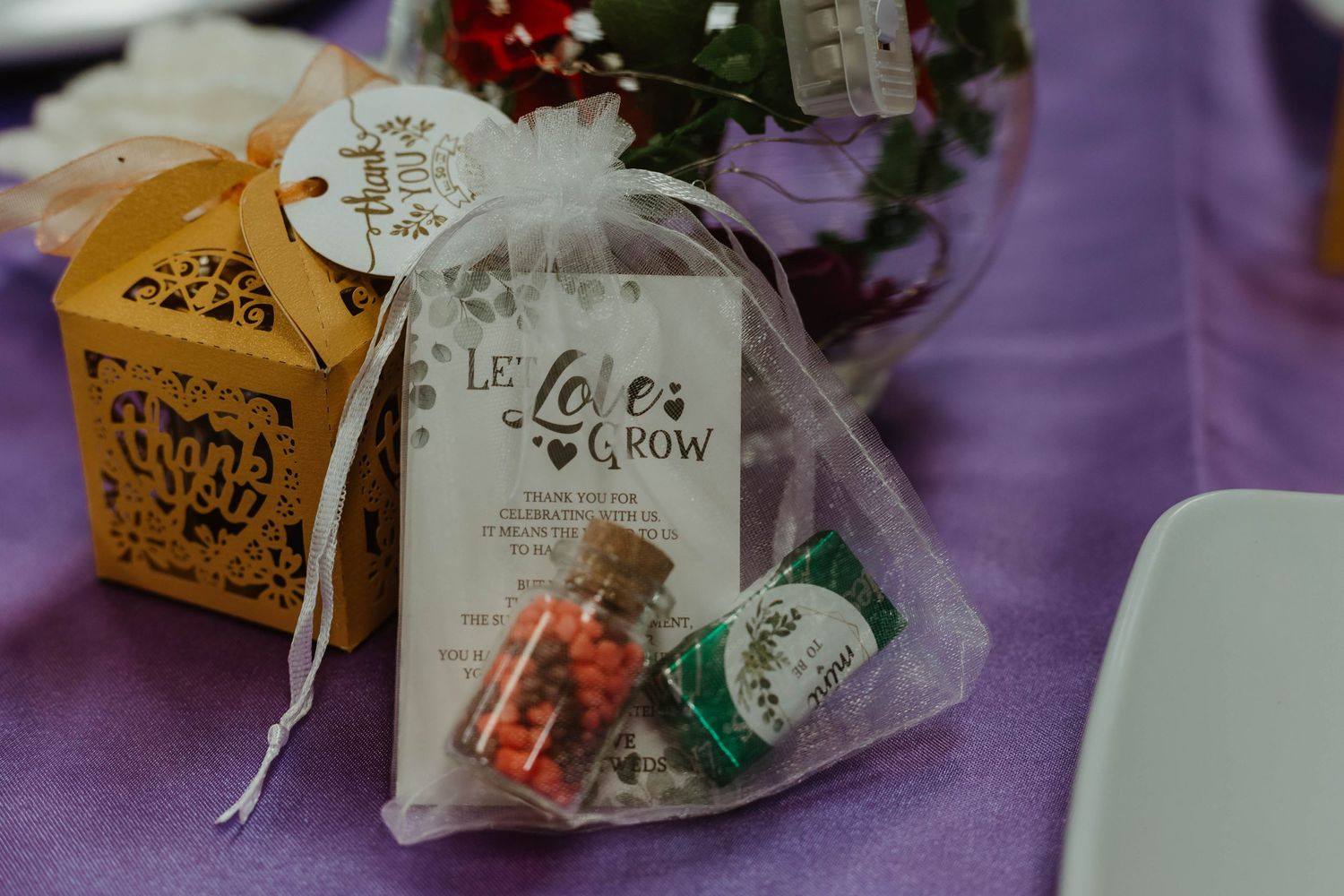 Wedding favor bags and decorative boxes displayed on purple tablecloth.