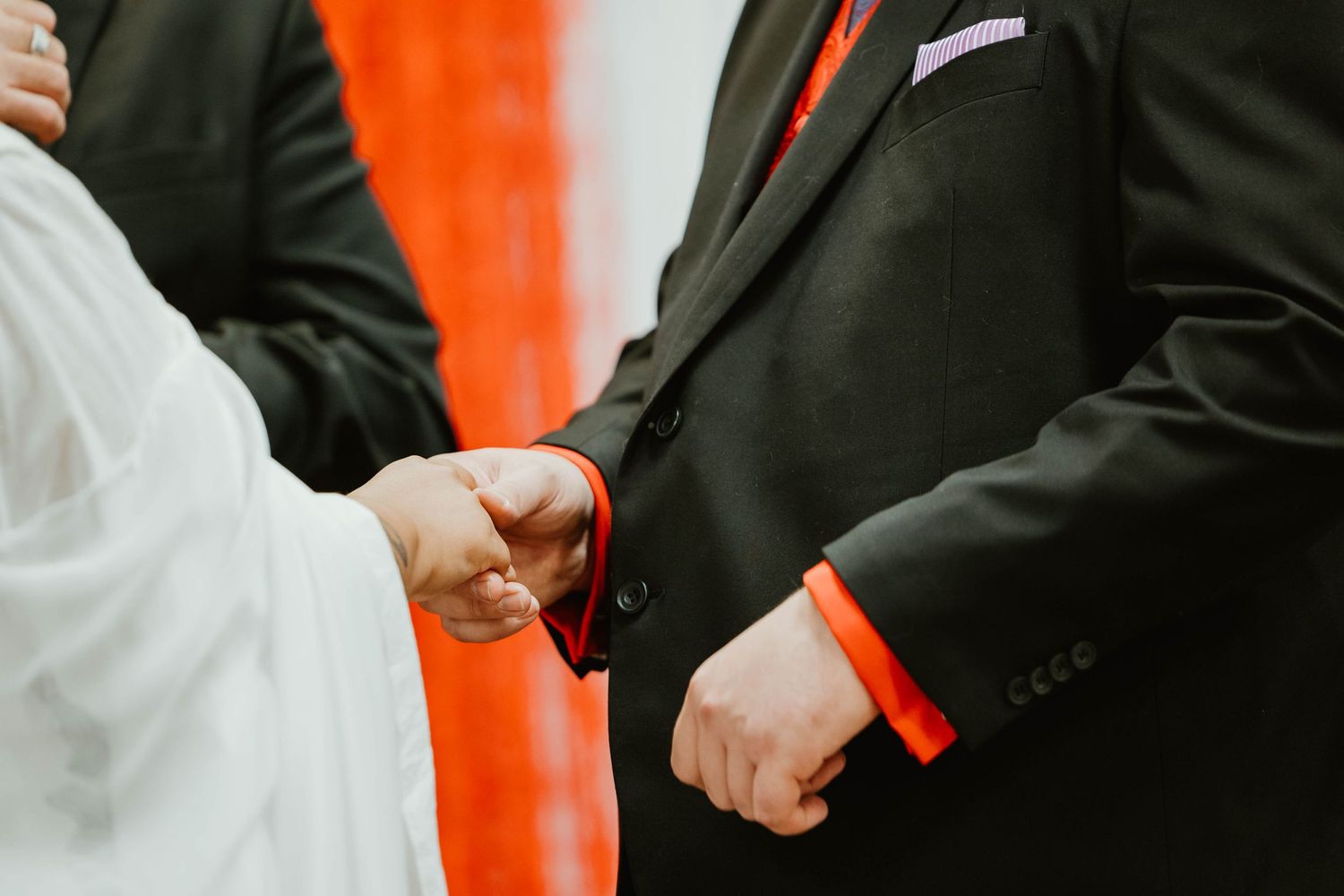 Close up of hands during wedding ring exchange ceremony with red and white backdrop.